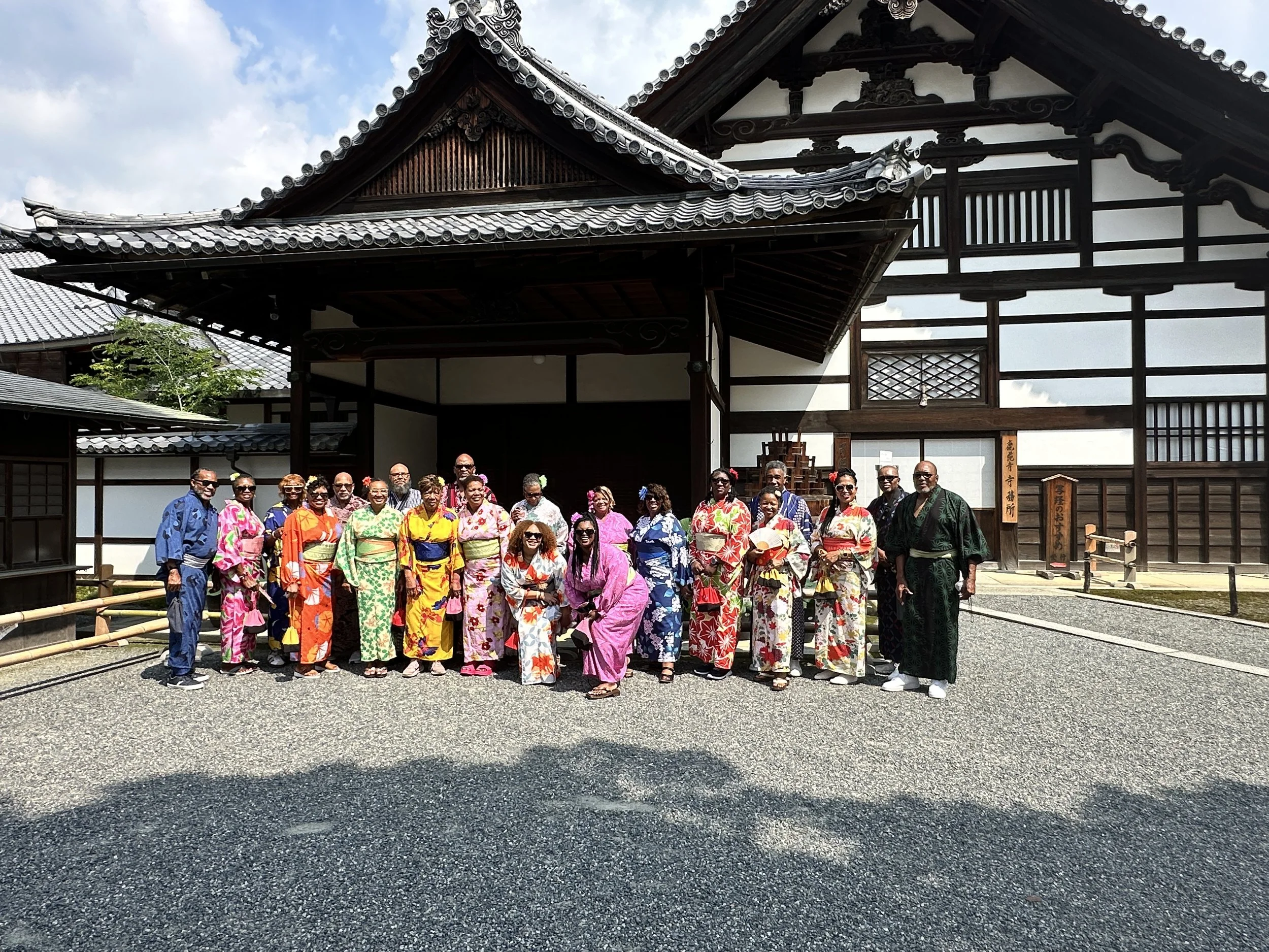 Group of people dressed in colorful traditional Japanese yukatas posing for a photo in front of a wooden temple building.