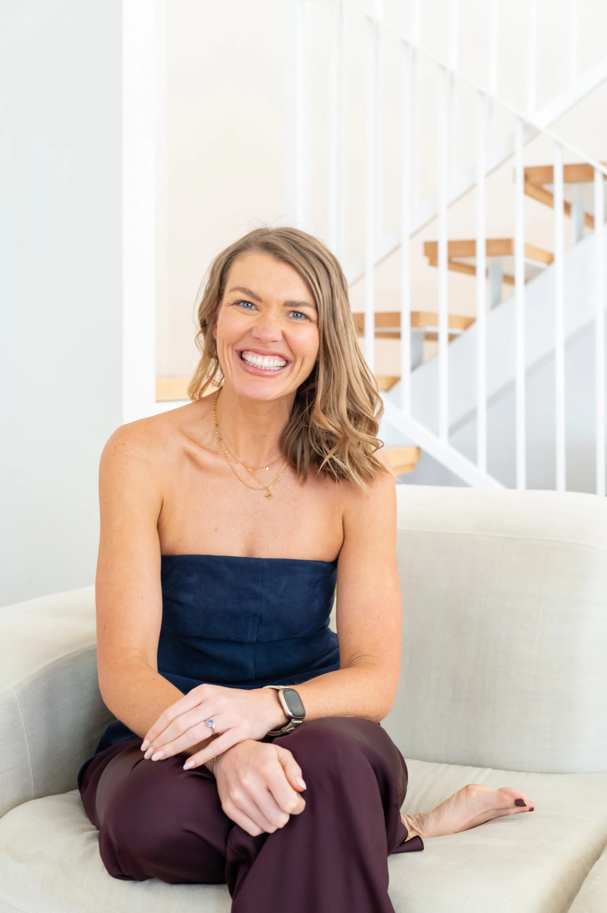 blonde woman sitting smiling in ble strapless top and maroon pants