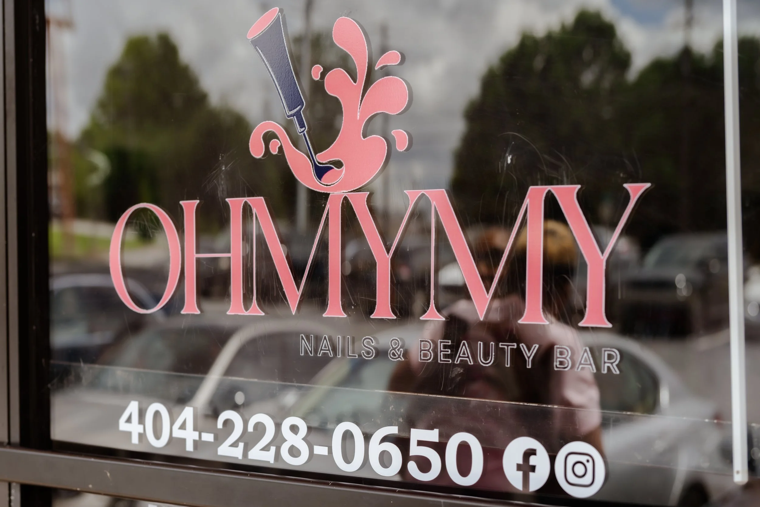 Sign for a nails and beauty bar featuring a pink nail polish bottle and stylized pink splash, with contact phone number and social media icons.