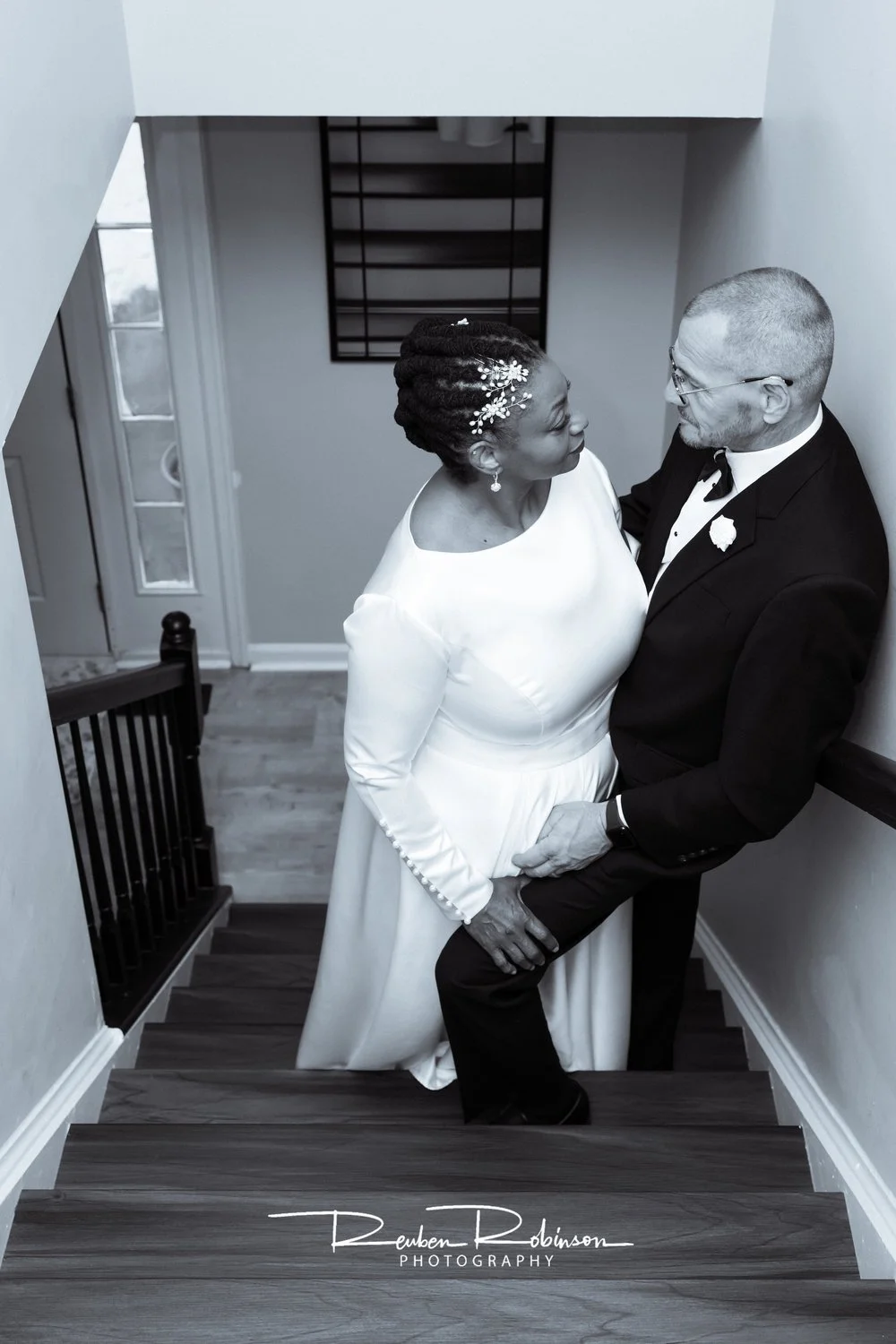 A bride and groom in wedding attire sharing an intimate moment on a staircase, holding hands and gazing at each other.