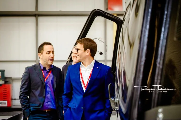 Three men in suits having a conversation indoors near a vehicle.