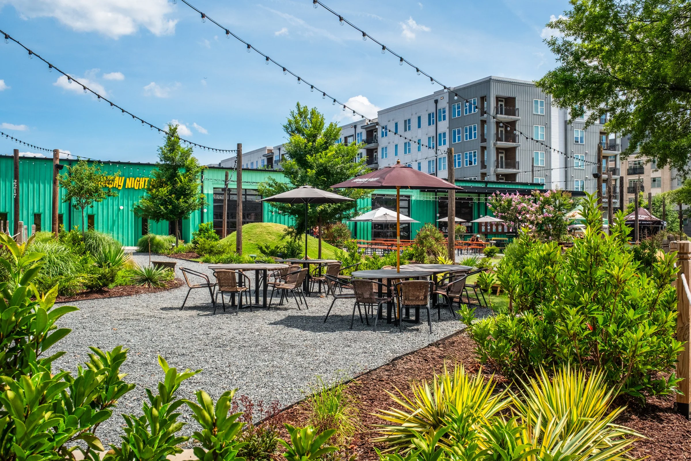 Architectural and landscape photography of Monday Night Brewing Charlotte, showcasing outdoor design, green spaces, and guest activity throughout the day.