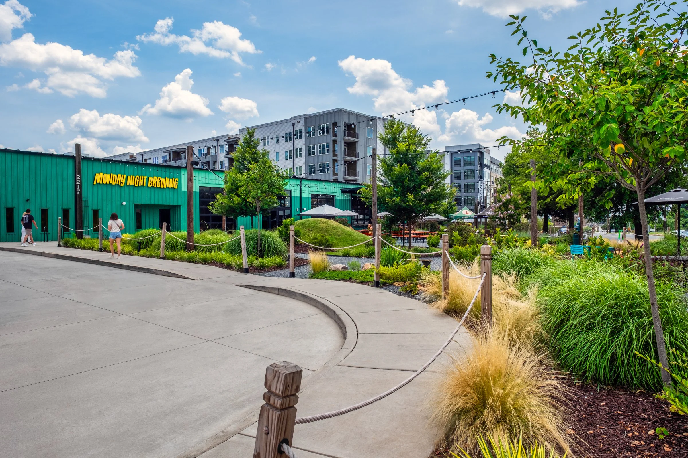 Architectural and landscape photography of Monday Night Brewing Charlotte, showcasing outdoor design, green spaces, and guest activity throughout the day.