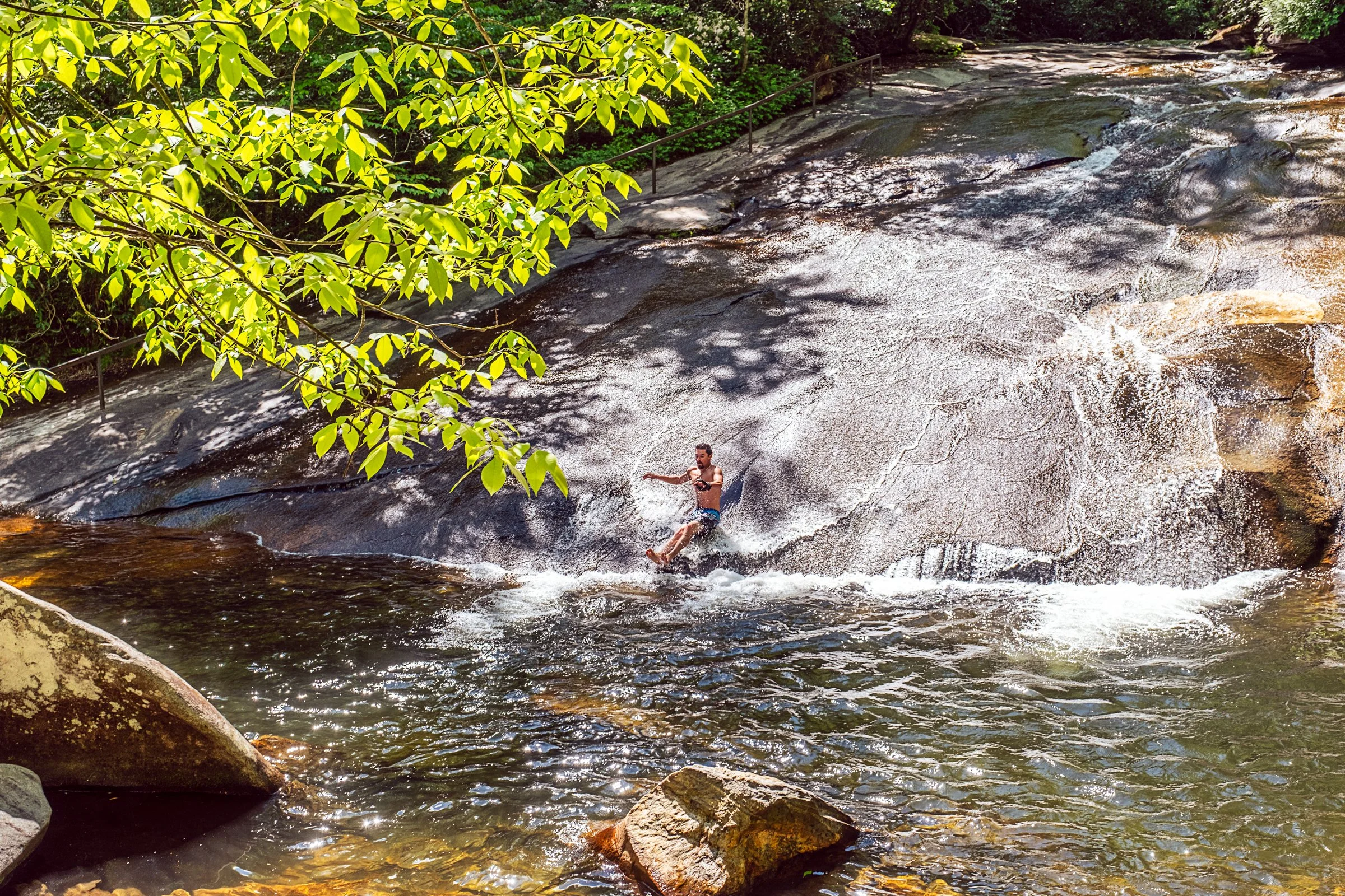 Visitors sliding down Sliding Rock, a natural granite waterslide in Pisgah National Forest near Asheville, North Carolina. Photographed by Lange Photo Studio. 