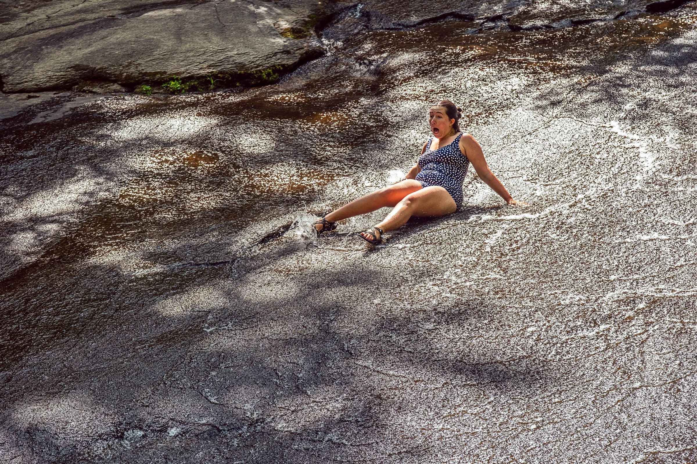 Visitors sliding down Sliding Rock, a natural granite waterslide in Pisgah National Forest near Asheville, North Carolina. Photographed by Lange Photo Studio. 