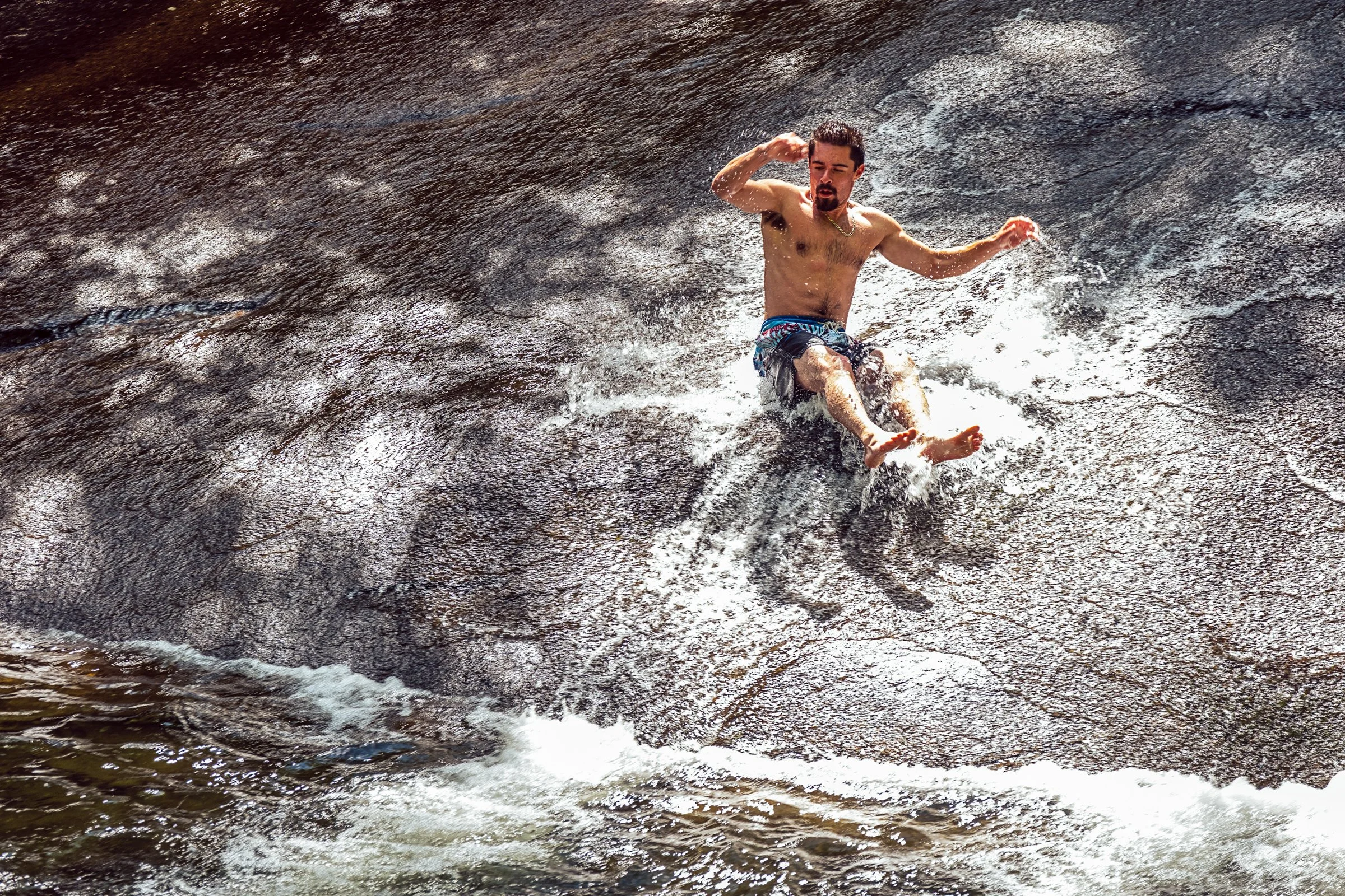 Visitors sliding down Sliding Rock, a natural granite waterslide in Pisgah National Forest near Asheville, North Carolina. Photographed by Lange Photo Studio. 