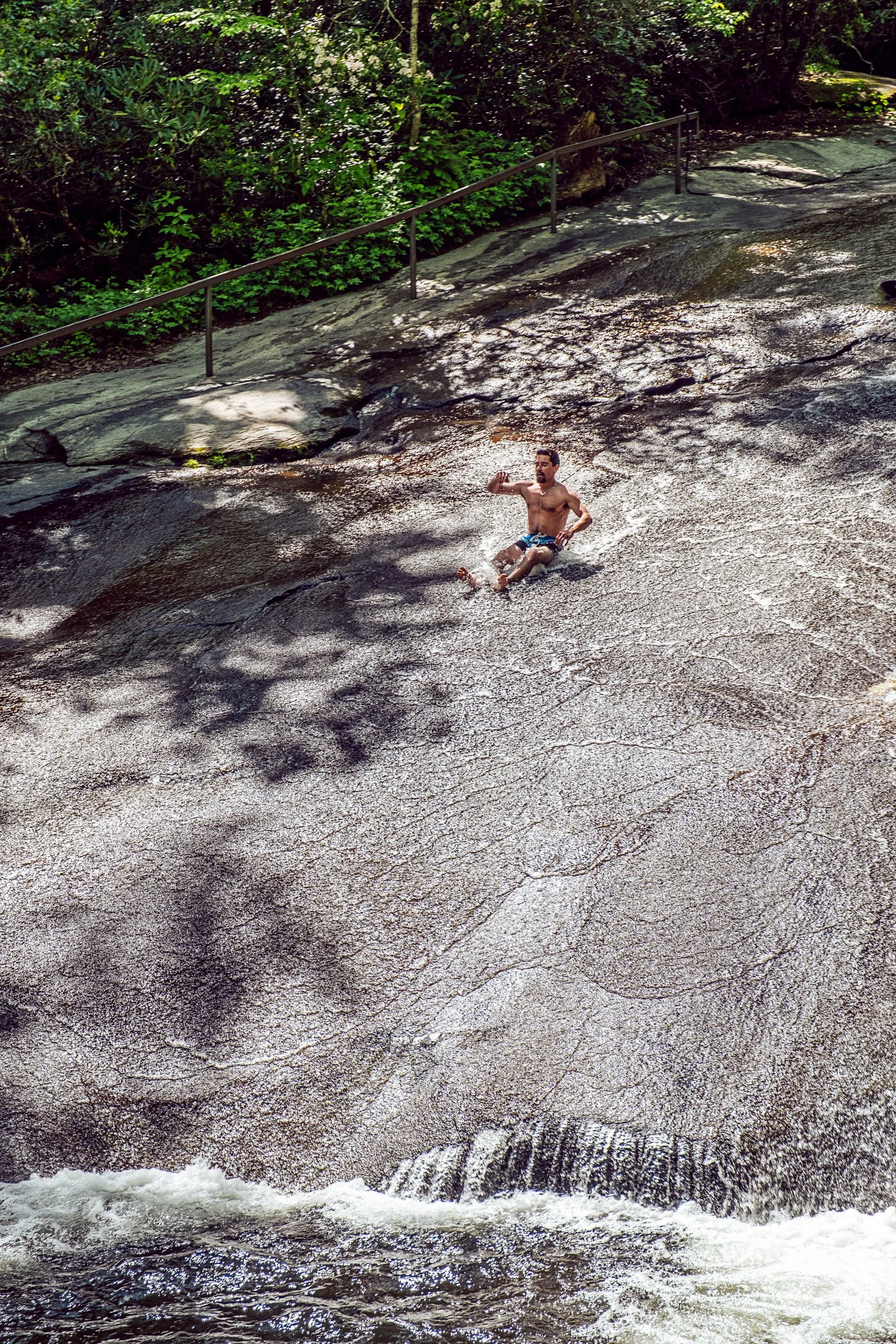 Visitors sliding down Sliding Rock, a natural granite waterslide in Pisgah National Forest near Asheville, North Carolina. Photographed by Lange Photo Studio. 