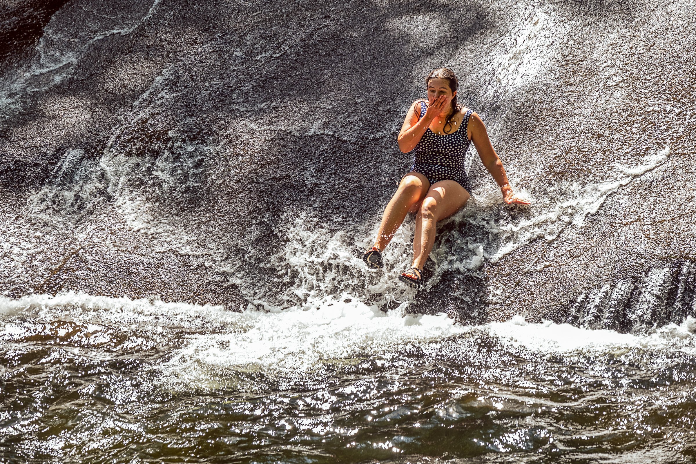 Visitors sliding down Sliding Rock, a natural granite waterslide in Pisgah National Forest near Asheville, North Carolina. Photographed by Lange Photo Studio. 