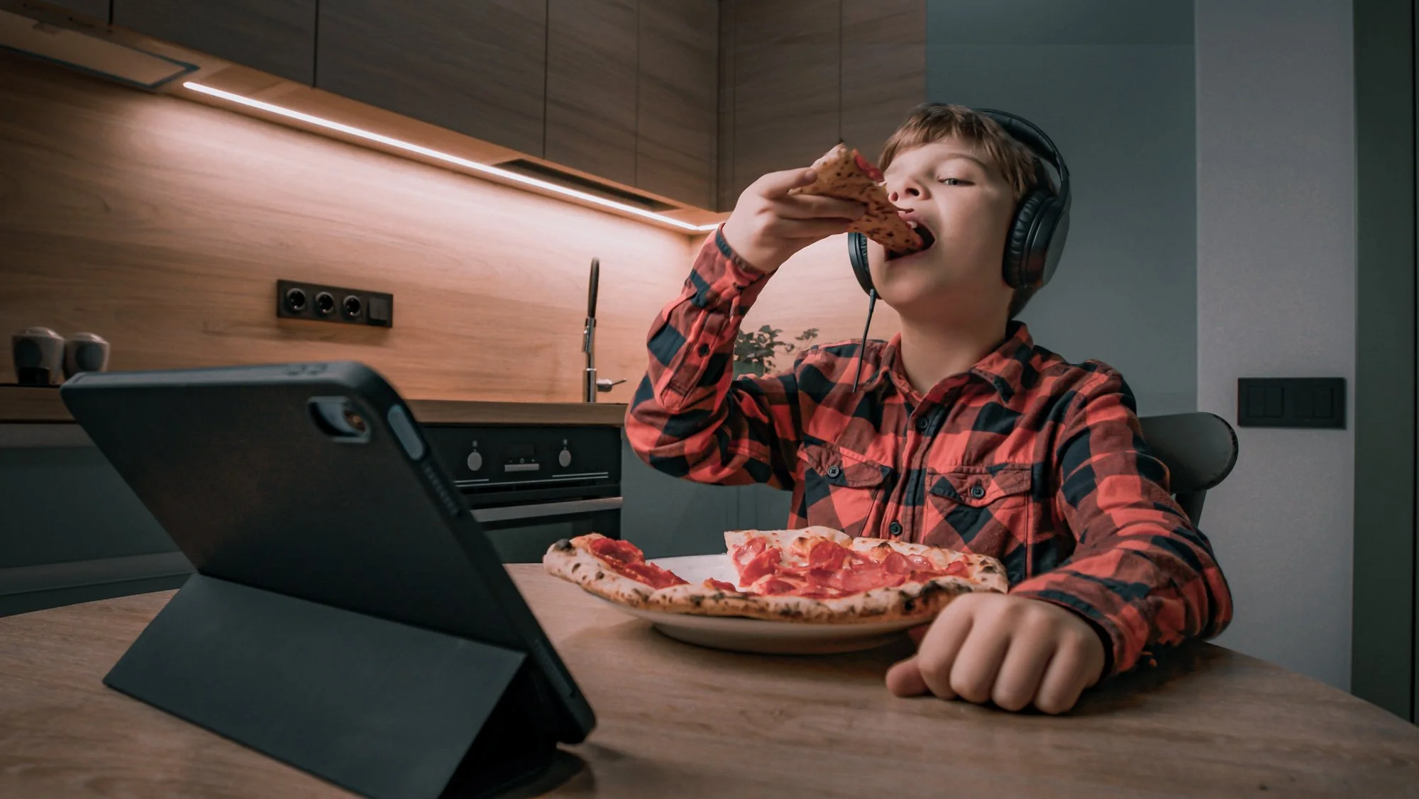 Autistic ADHD child eating with headphones to block out sound as he has sensory sensitivities with loud noise at dinner time