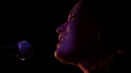 A woman singing into a microphone with a dark background.