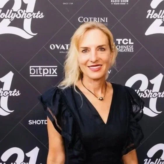 A woman with blonde hair and a black dress standing in front of a black backdrop with logos for Hollywood Shorts, Cotrini, TCL Chinese Theatres, and BitPix.
