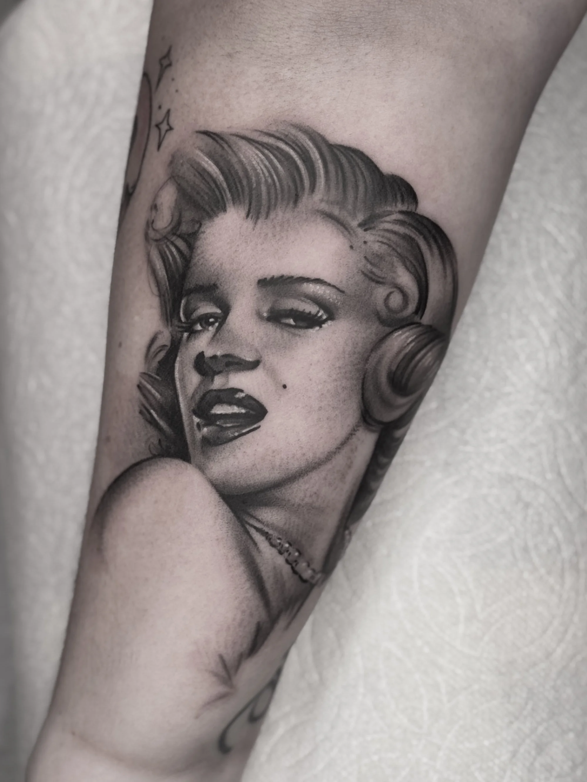 Black and gray realism tattoo of a woman's portrait with styled hair, lipstick, and a necklace.