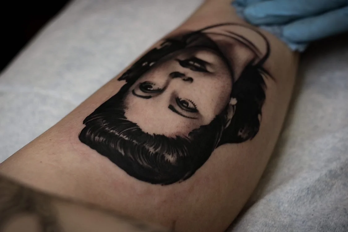 Black and grey portrait tattoo of a woman with short hair on person's arm.