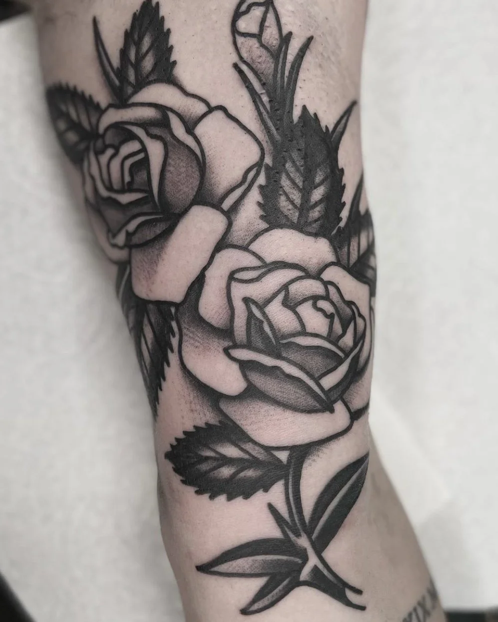 A black and gray tattoo of two roses surrounded by leaves on a person's arm.