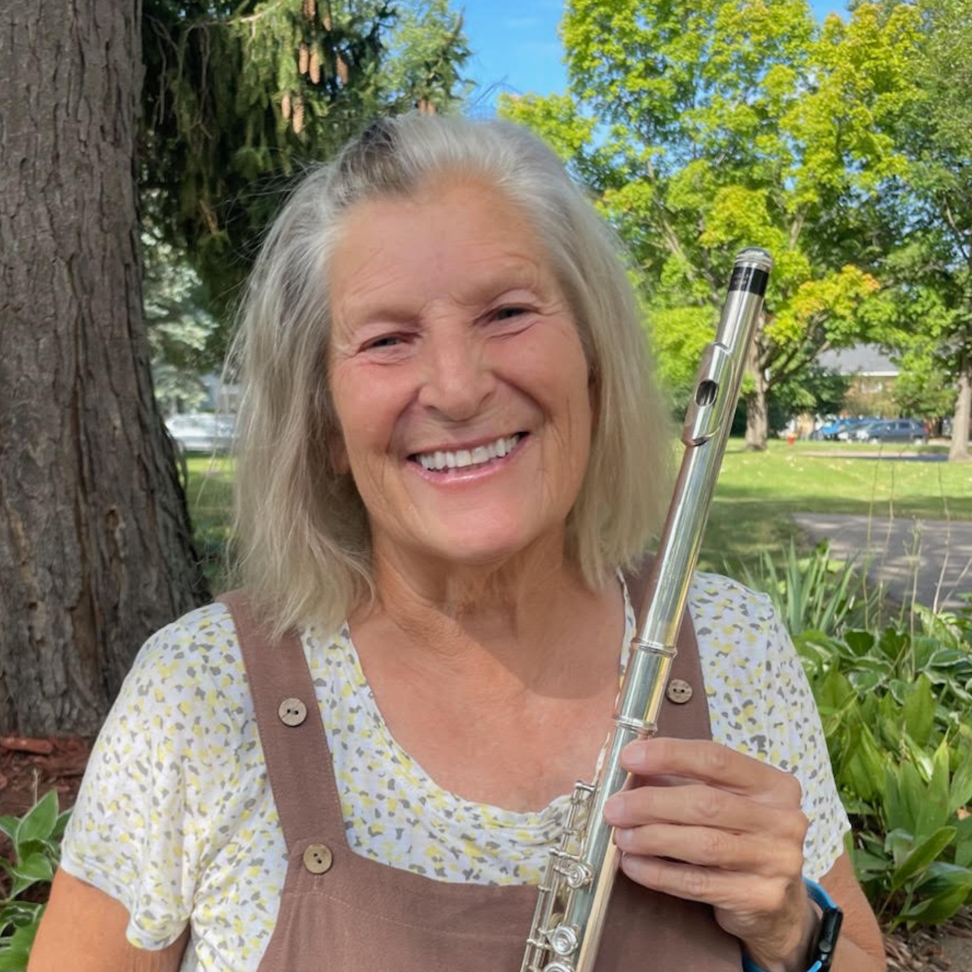 A portrait of an elderly woman with shoulder-length gray hair, smiling, wearing a black top and a colorful patterned scarf.
