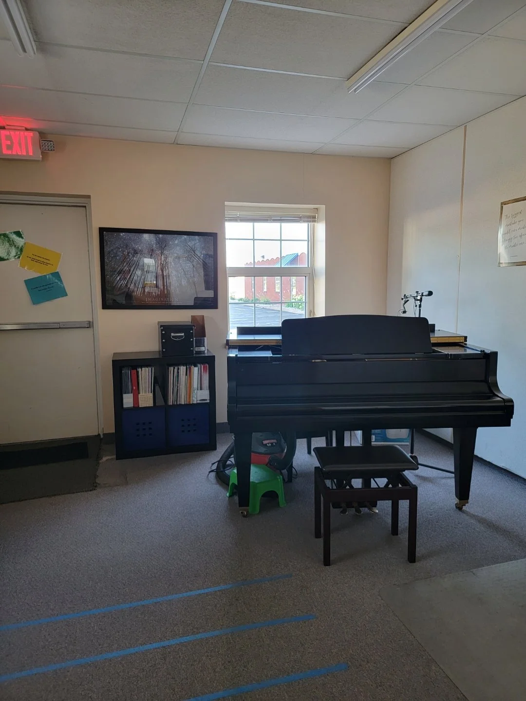 A room with a black grand piano, a window, a bookshelf, and wall decor.