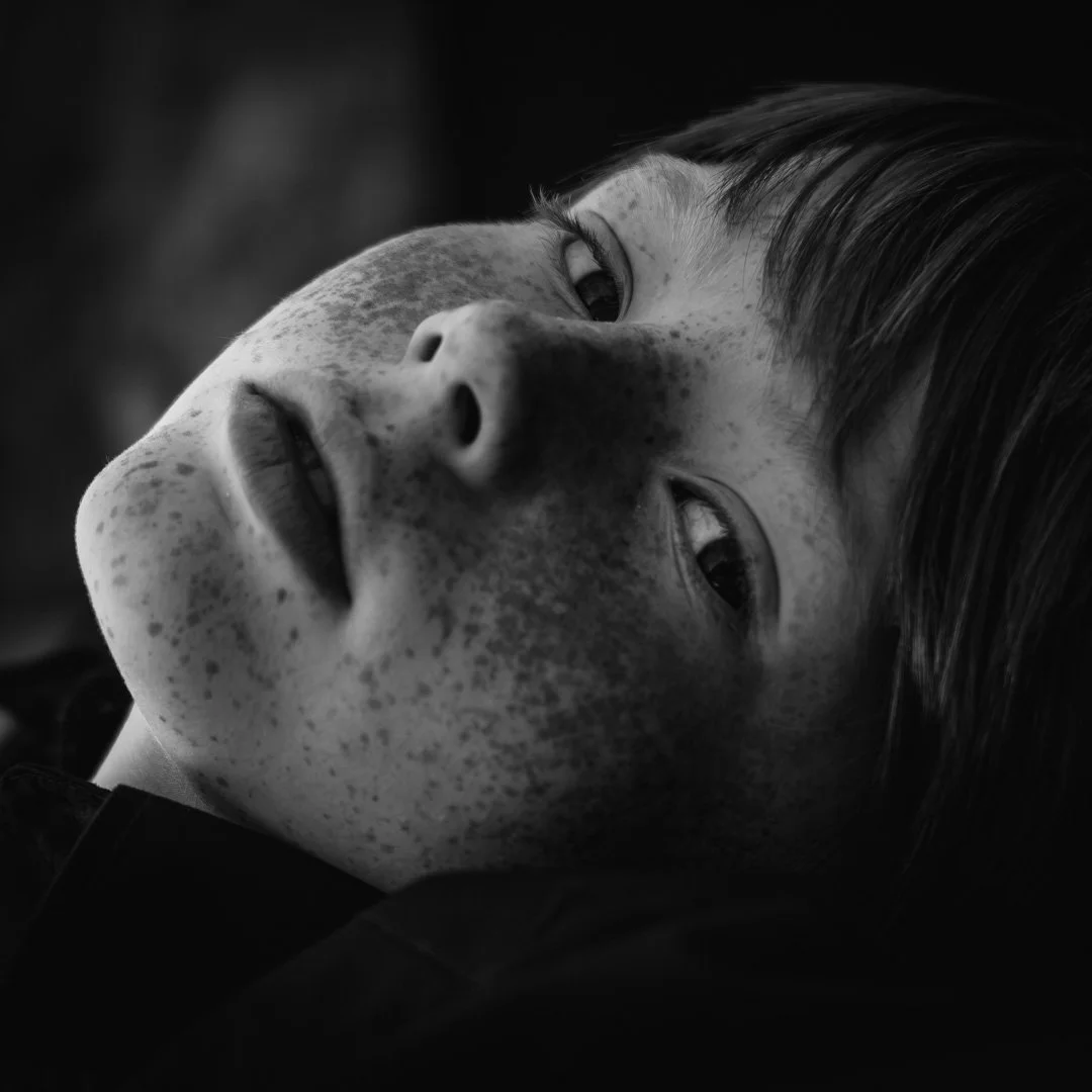 Close-up black and white portrait of a child's face with freckles, lying down and gazing upwards.