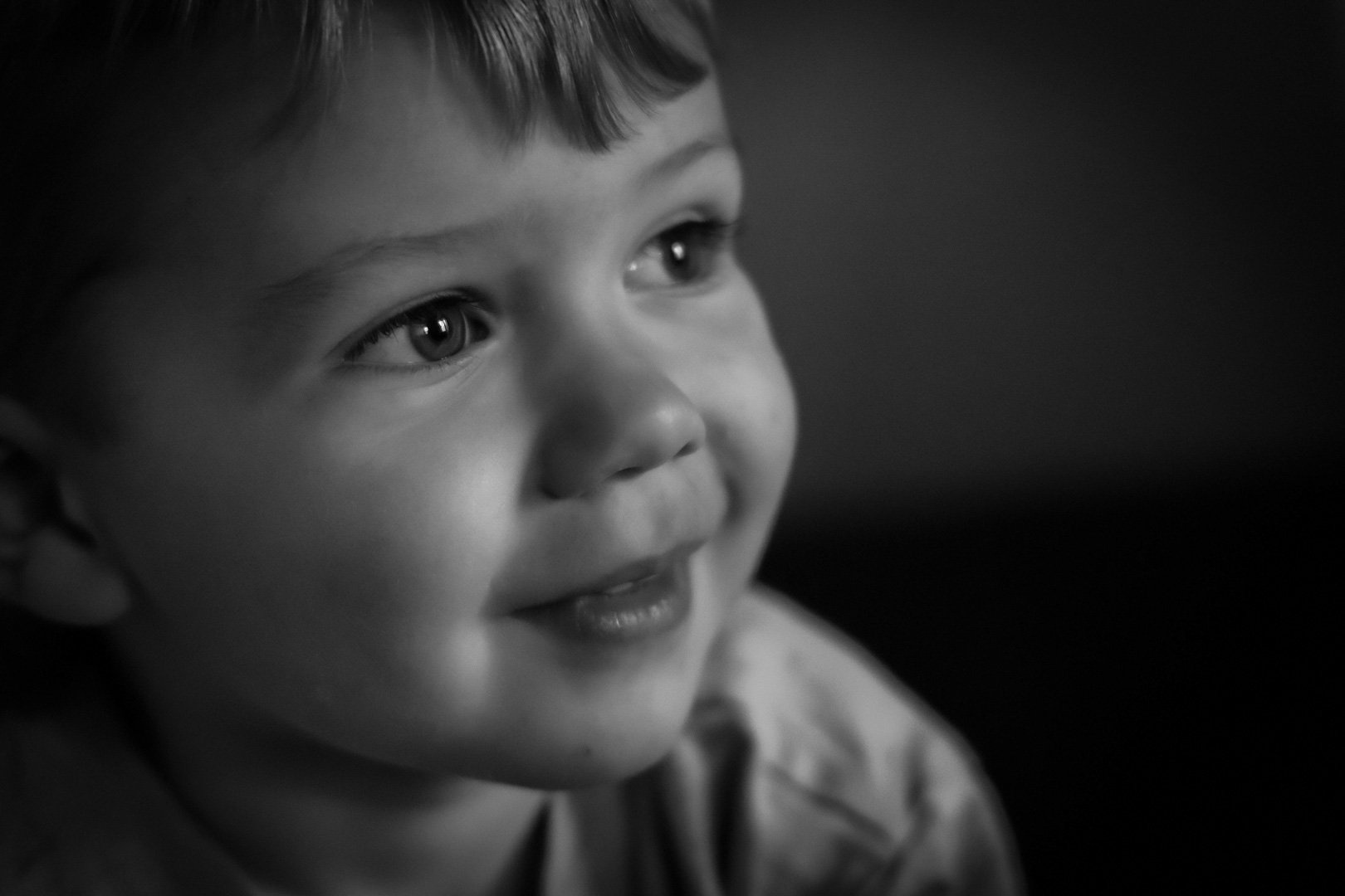 Close-up of a little boy's face in black and white, showing a joyful expression with bright eyes and a faint smile.