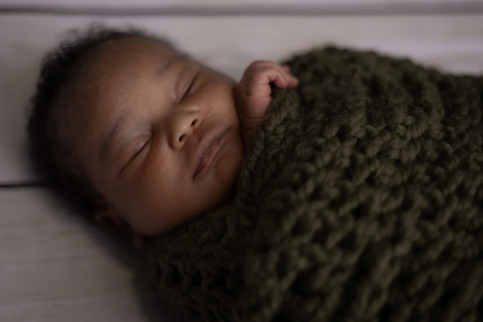 sleeping baby wrapped in green knit blanket.