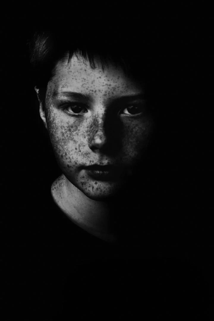 black and white portrait of a boy with freckles, staring intensely at the camera, with dramatic lighting 