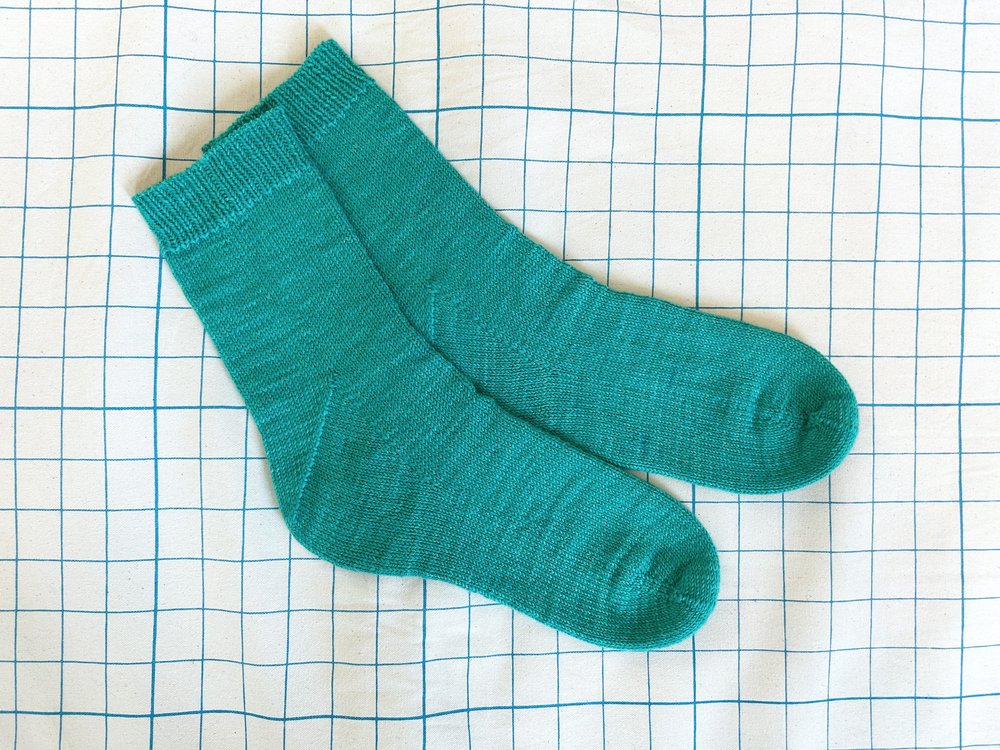 A pair of turquoise knit socks with a grid backdrop.