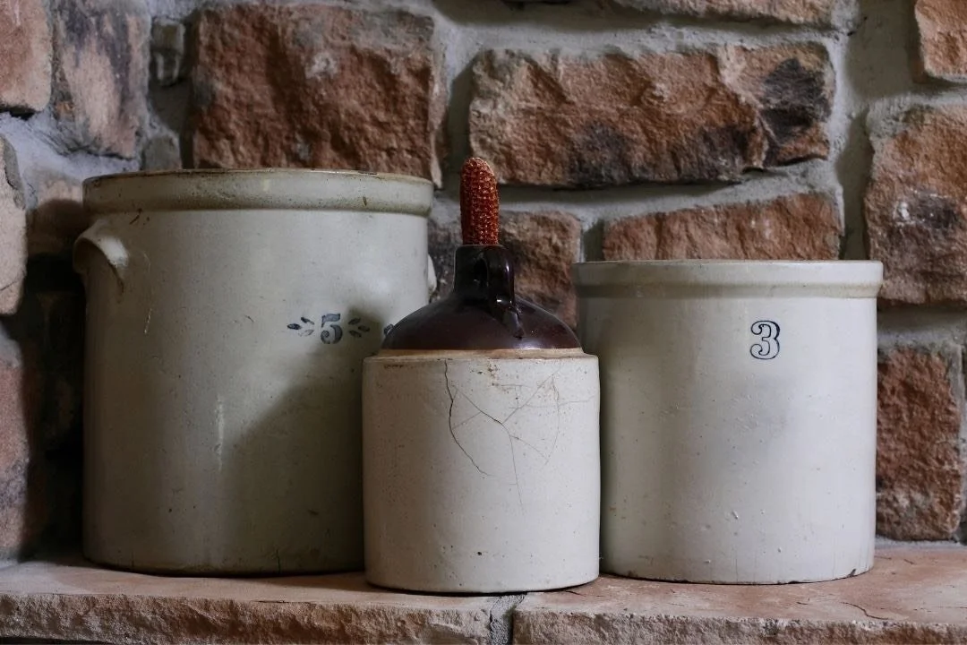 Three old stone fermentation crocks on a brick ledge against a red brick wall.