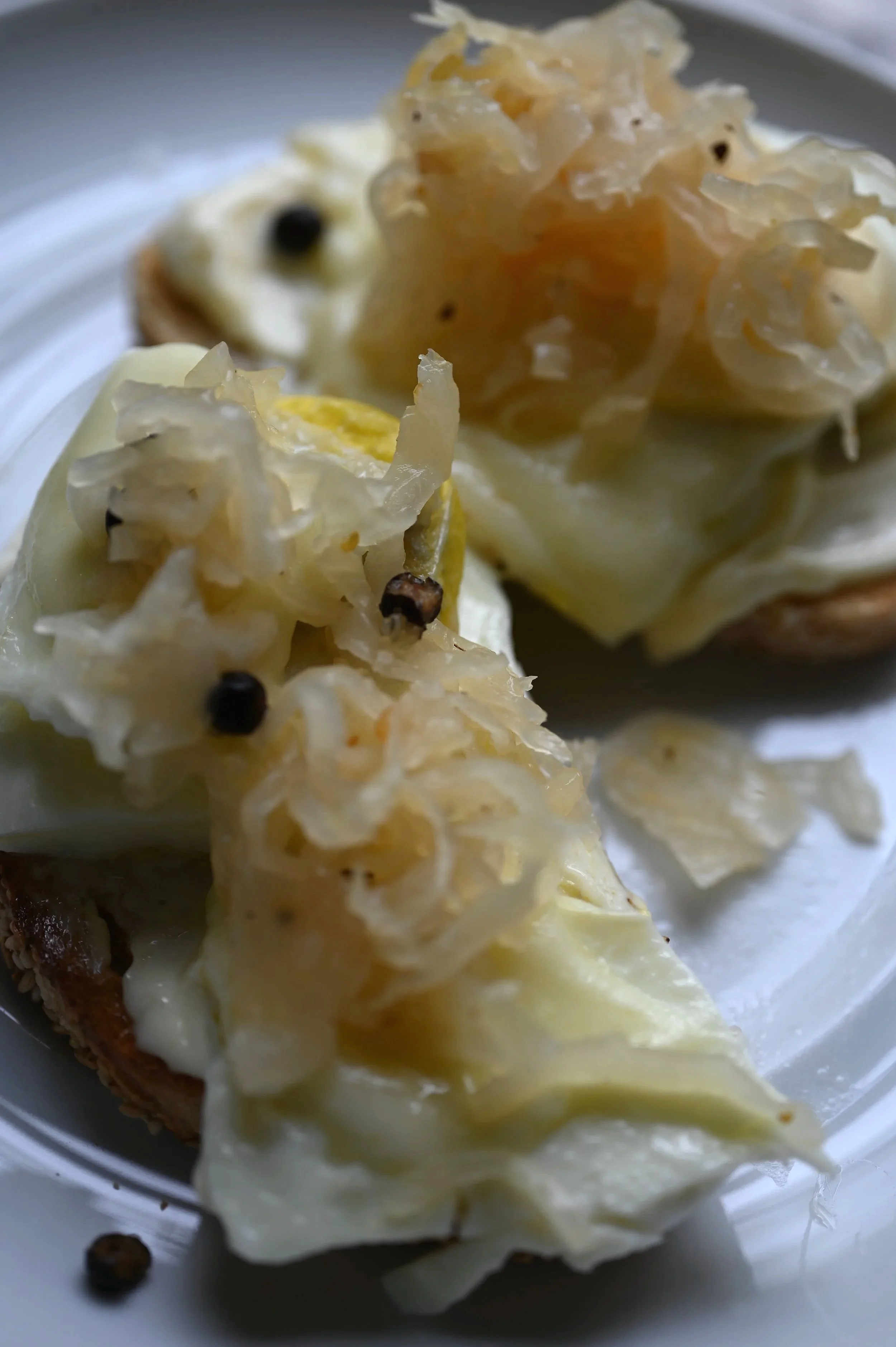 Kraut toast starting with sourdough then layered with an egg over hard and topped with apple juniper berry and garlic sauerkraut served on a white plate.