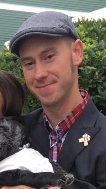 A woman with long brown hair smiling, outdoors during sunset.