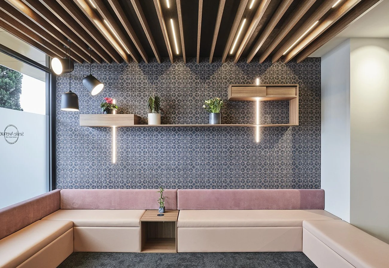 Modern interior with a pink and beige L-shaped sofa, decorative wall with patterned wallpaper, hanging pendant lights, and wooden shelves with plants.
