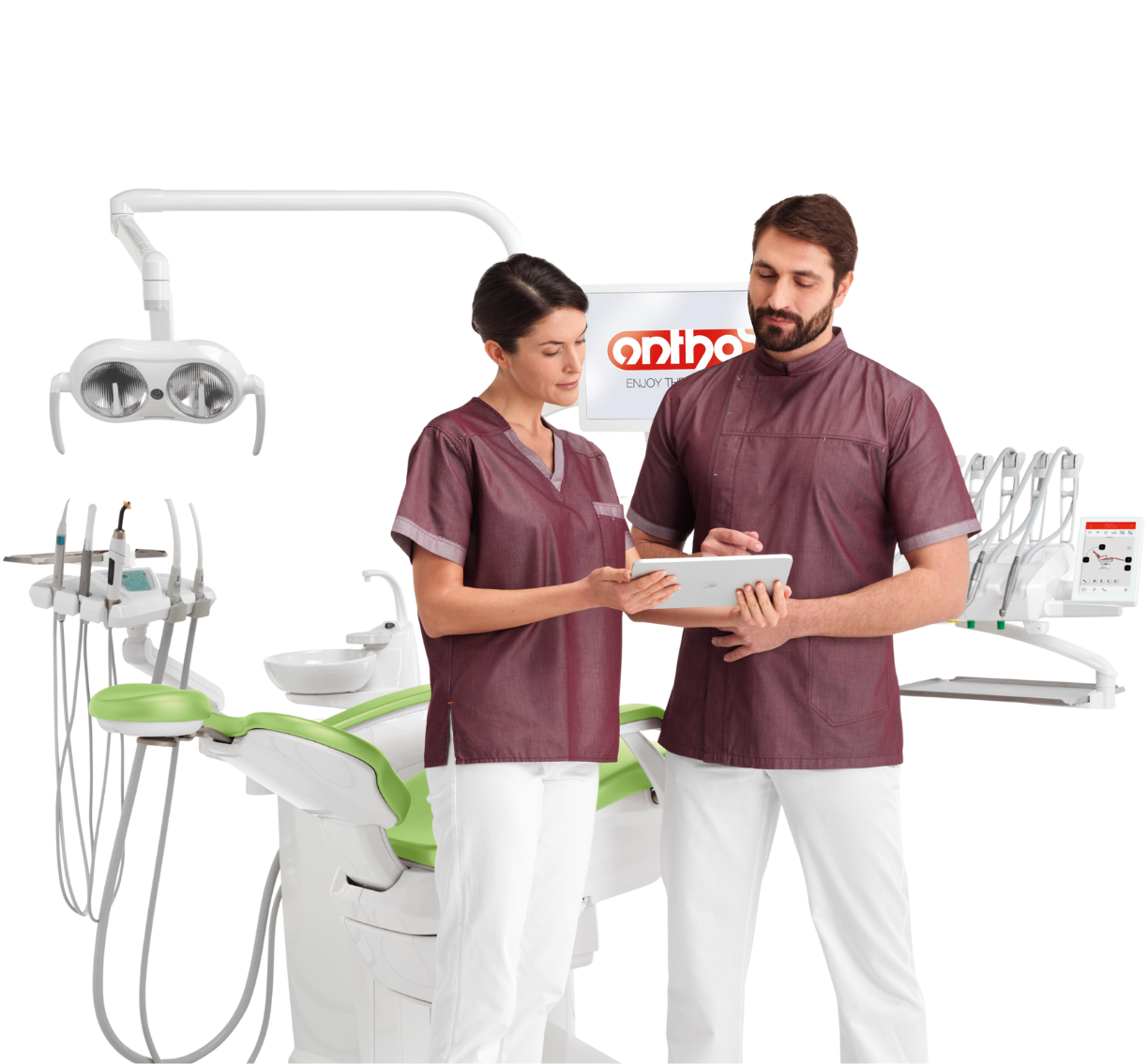 Two dental professionals, a woman and a man, standing in a dental clinic, reviewing information on a tablet, with dental equipment and a dental chair in the background.