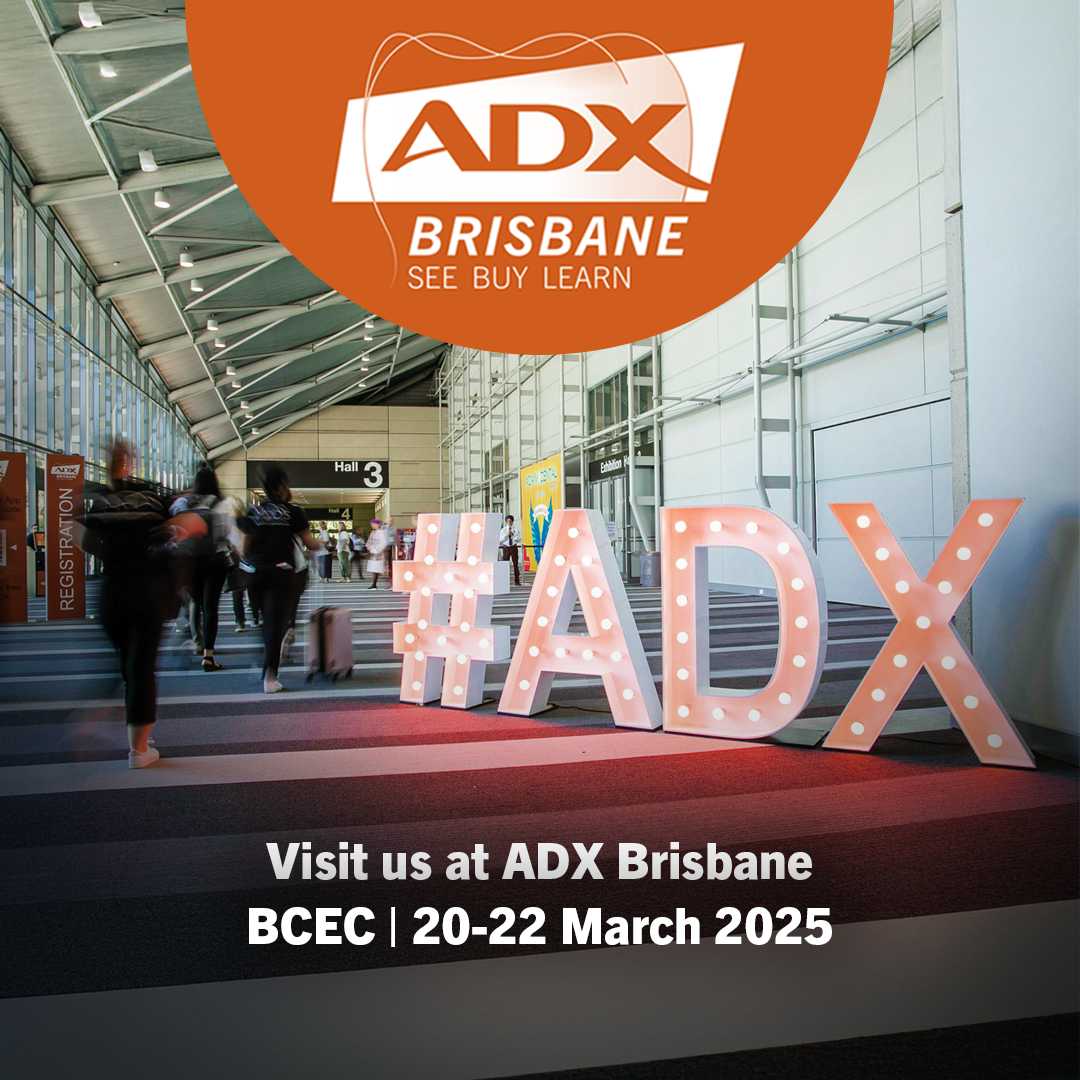 Large illuminated '#ADX' letters in a convention center, promoting the ADX Brisbane event at BCEC, March 20-22, 2025. People are walking in the hallway.