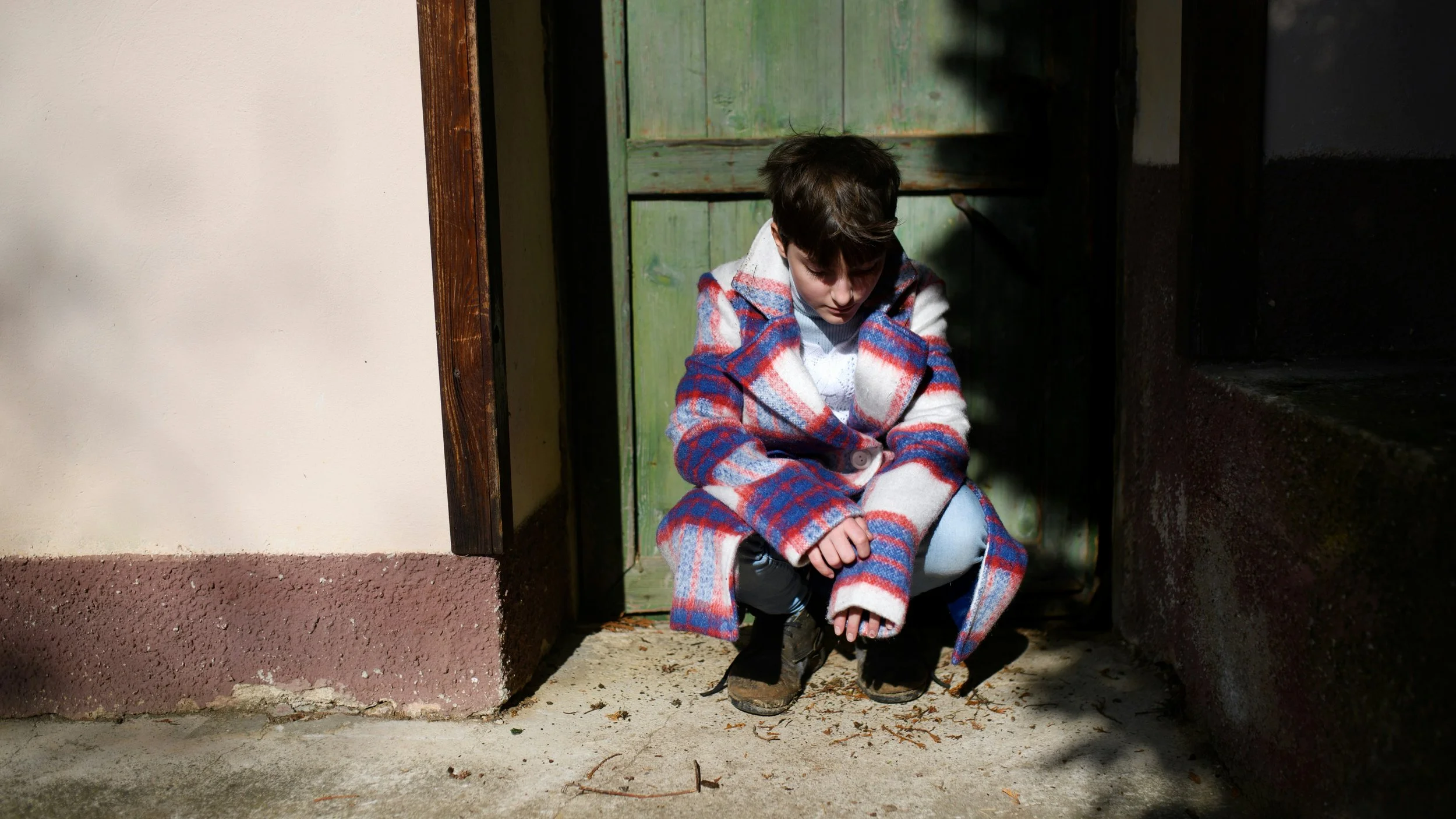 teenager squatting outside a door and looking at the ground