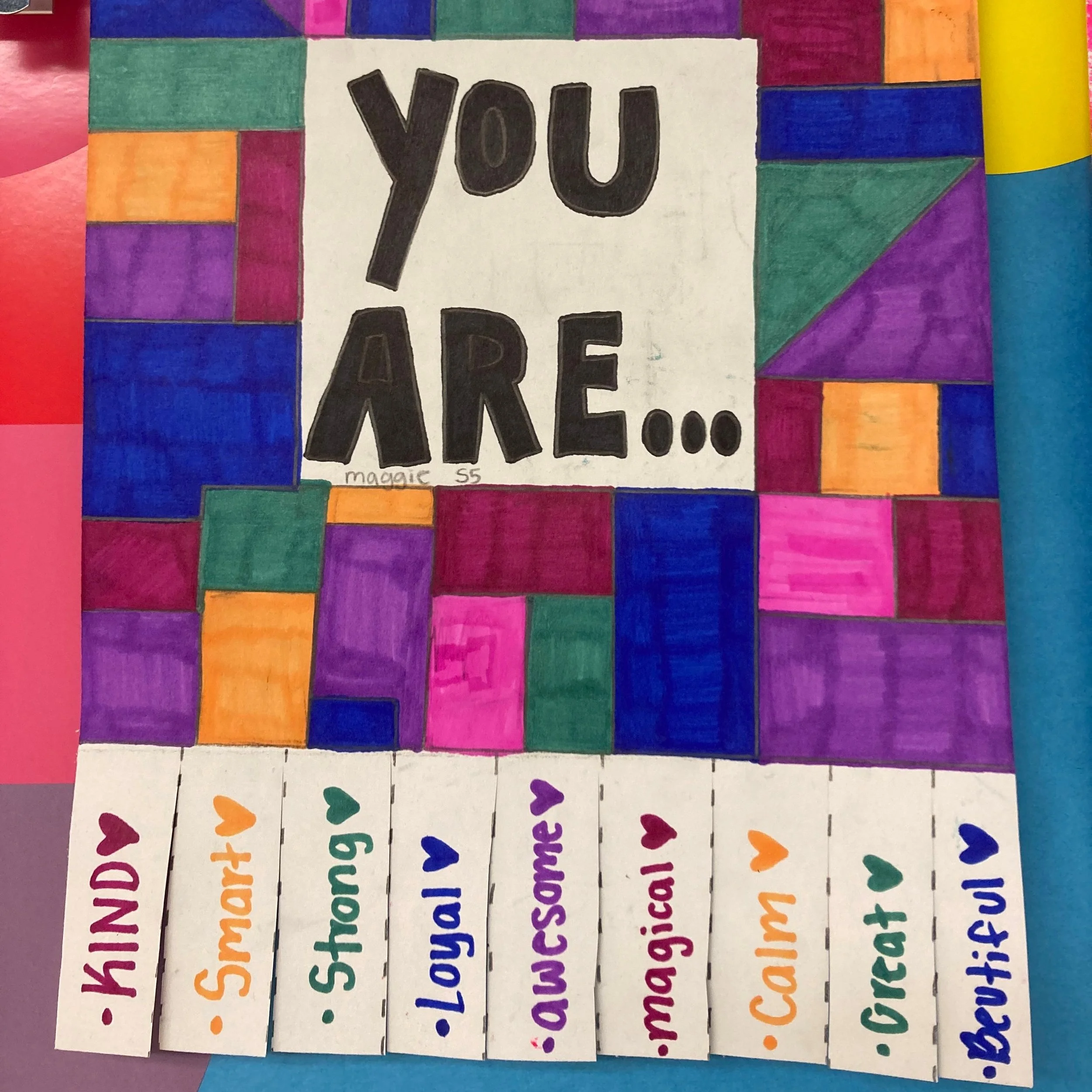Colorful handmade poster with a grid of small rectangles in various colors, with the phrase 'You Are...' in bold black letters in the center. Below, there are strips of paper with words such as 'Kind,' 'Smart,' 'Strong,' 'Loyal,' 'Awesome,' 'Magical,