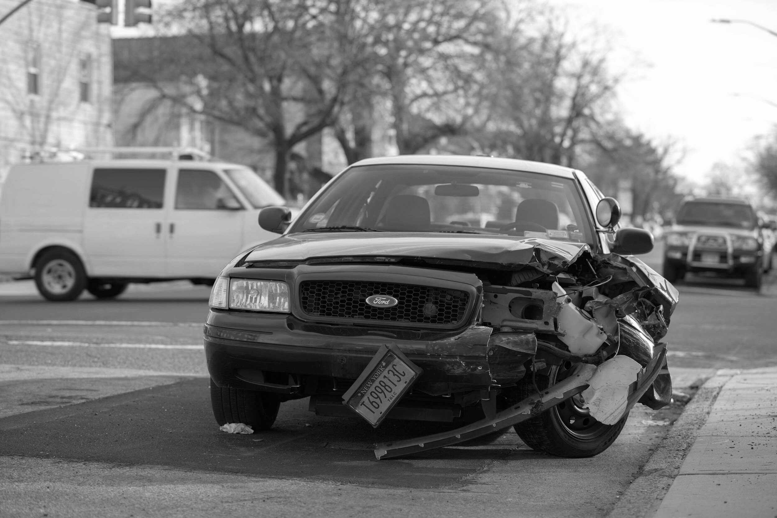 Car with damaged front end after an accident, license plate visible, parked on roadside.