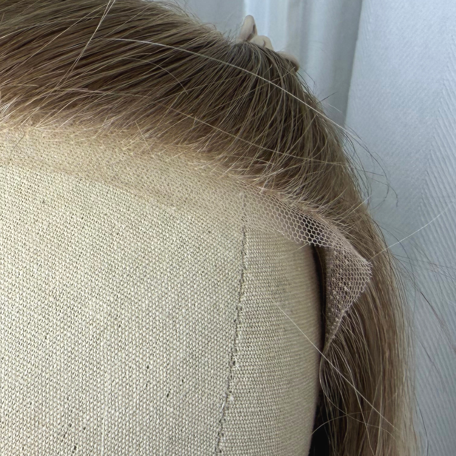 Close-up of a beige upholstered chair with fabric tape on the edge, with a person's blonde hair visible in the background.
