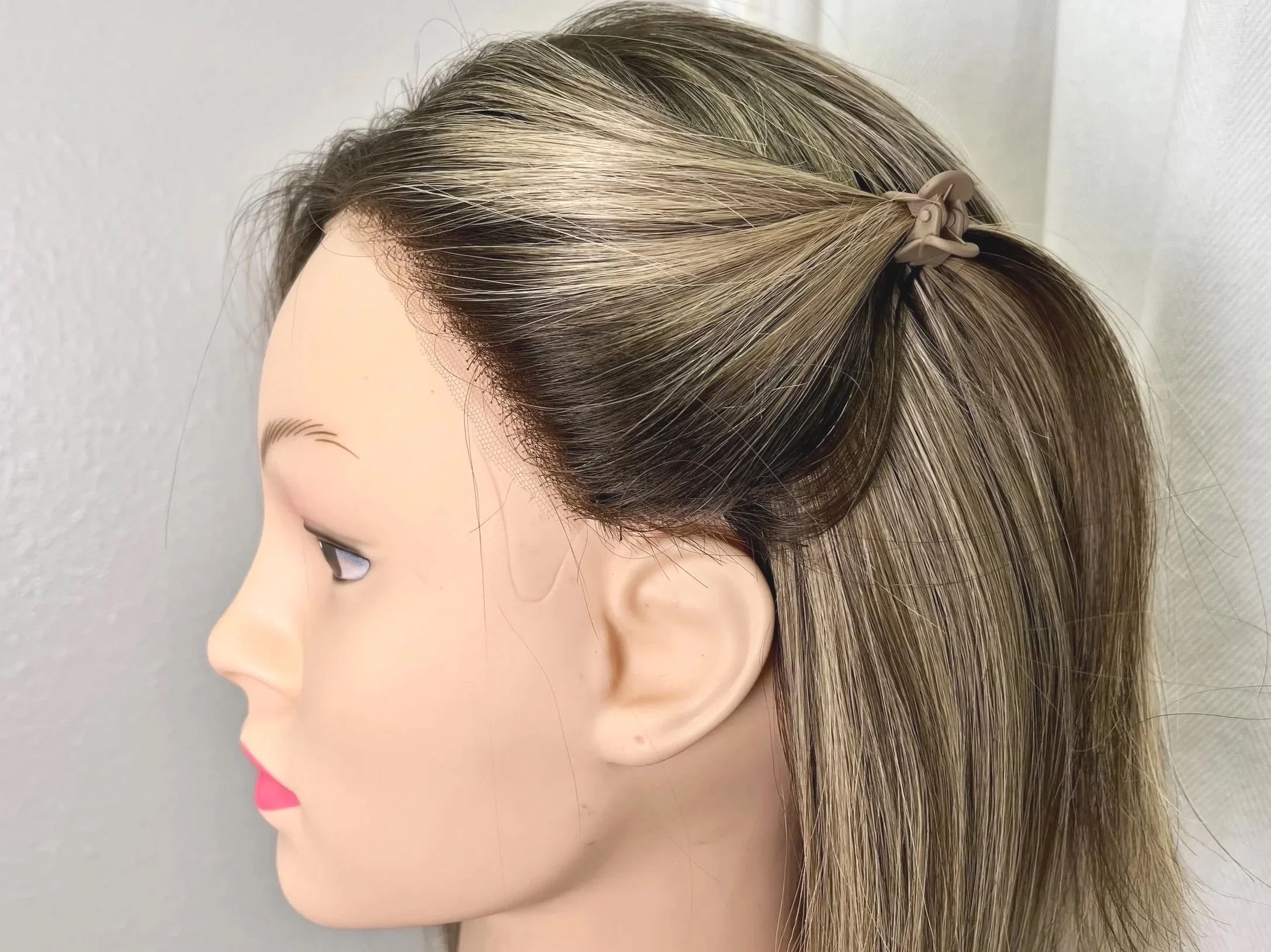 A mannequin head with blonde hair styled in a half-up, half-down hairstyle secured with a beige bow hair clip.