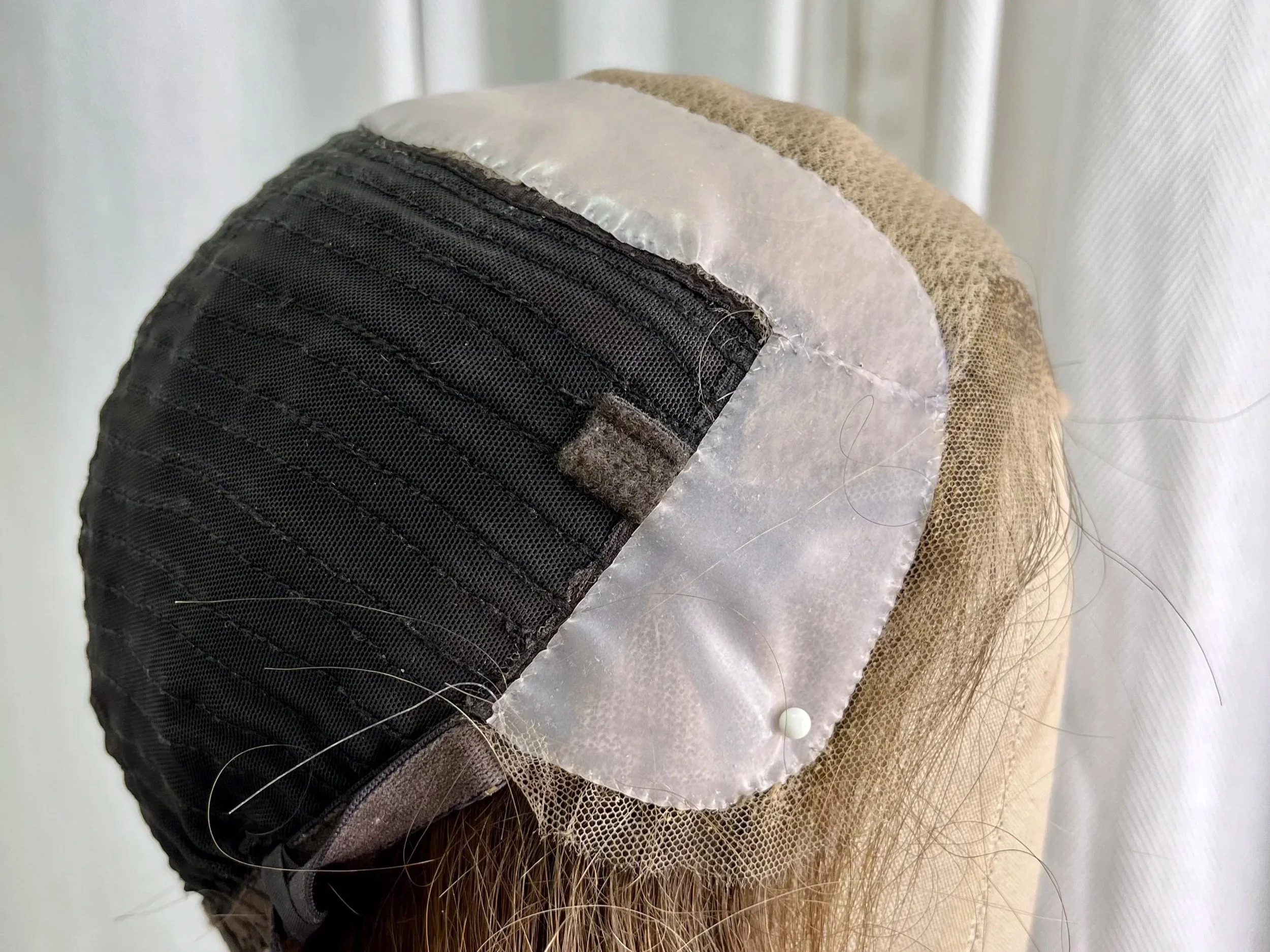 A wig with a black hairnet and a lace front, attached to a mannequin head, showing the hairline and scalp area.