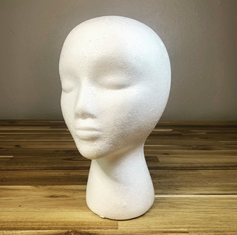 White foam mannequin head with closed eyes on wooden surface.