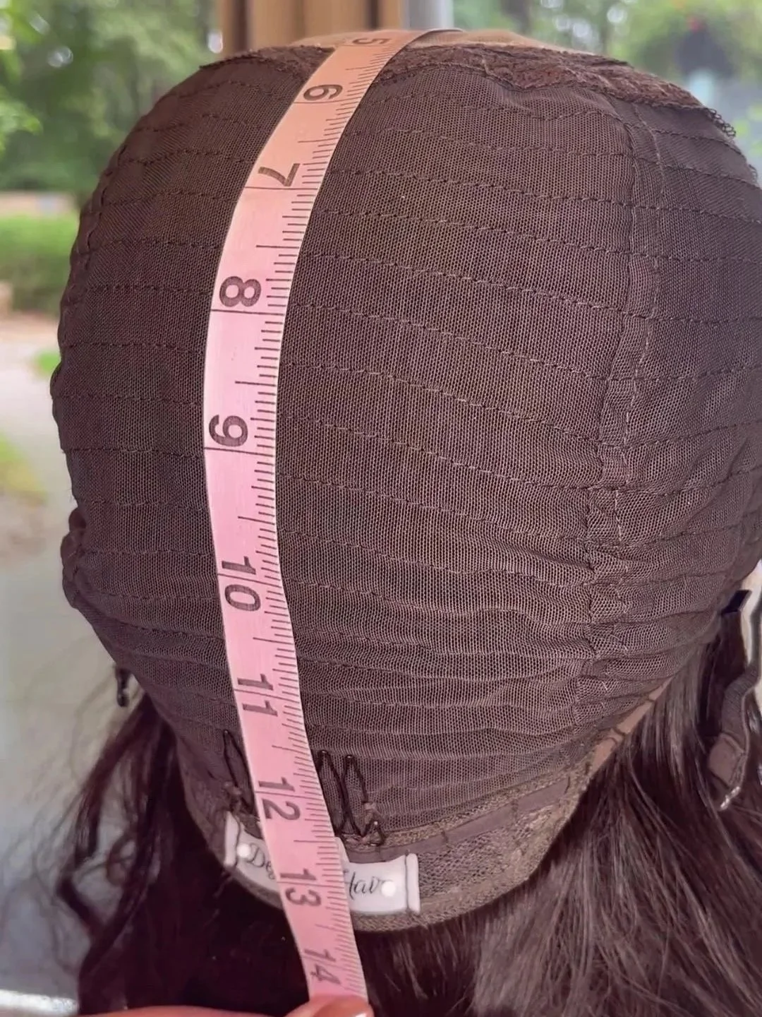 Close-up of the inside of a wig on a mannequin head, with a pink measuring tape indicating approximately 14 inches in length.
