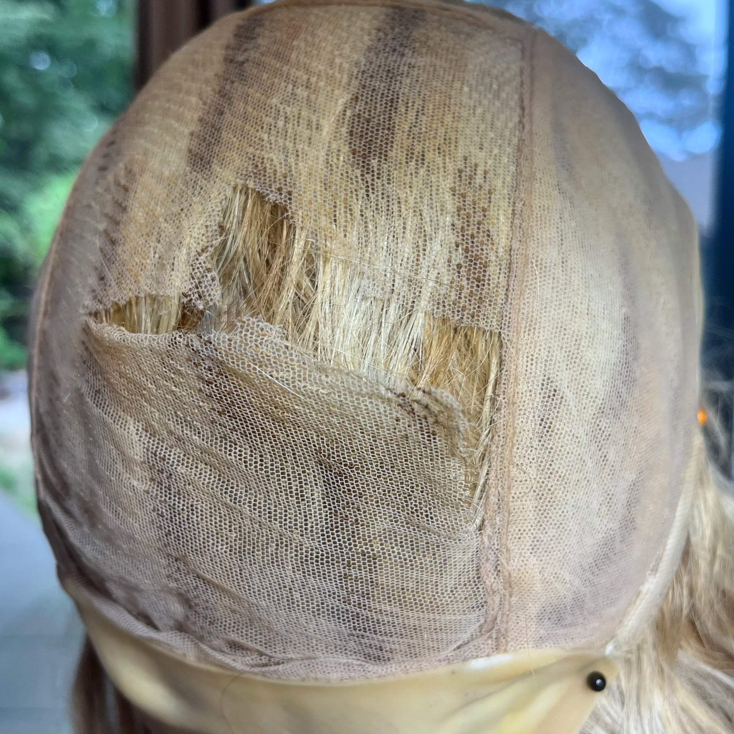 Back of a hand tied lace cap wig that has a large tear.