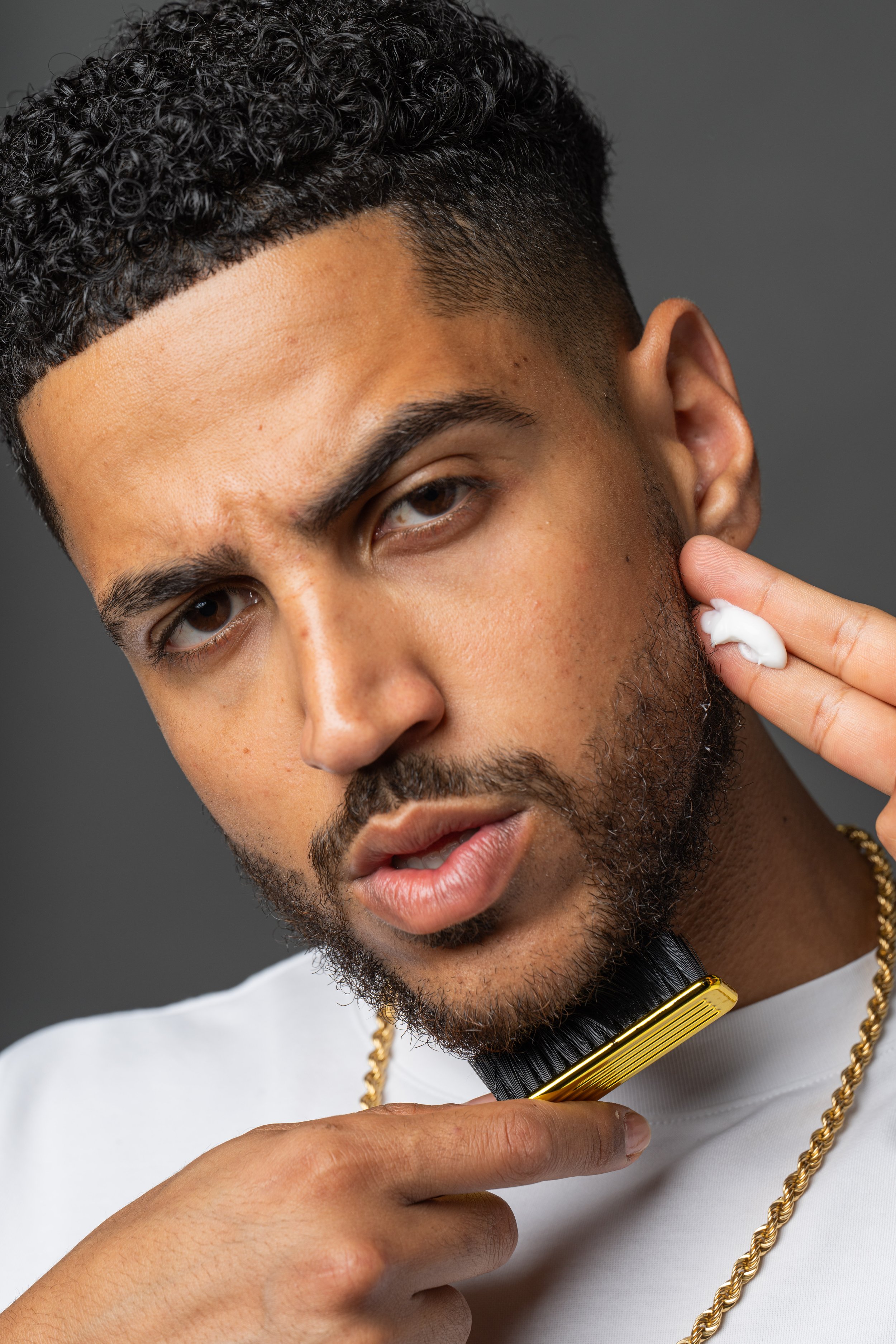 Young man applying skincare while holding beard comb during men's grooming lifestyle shoot