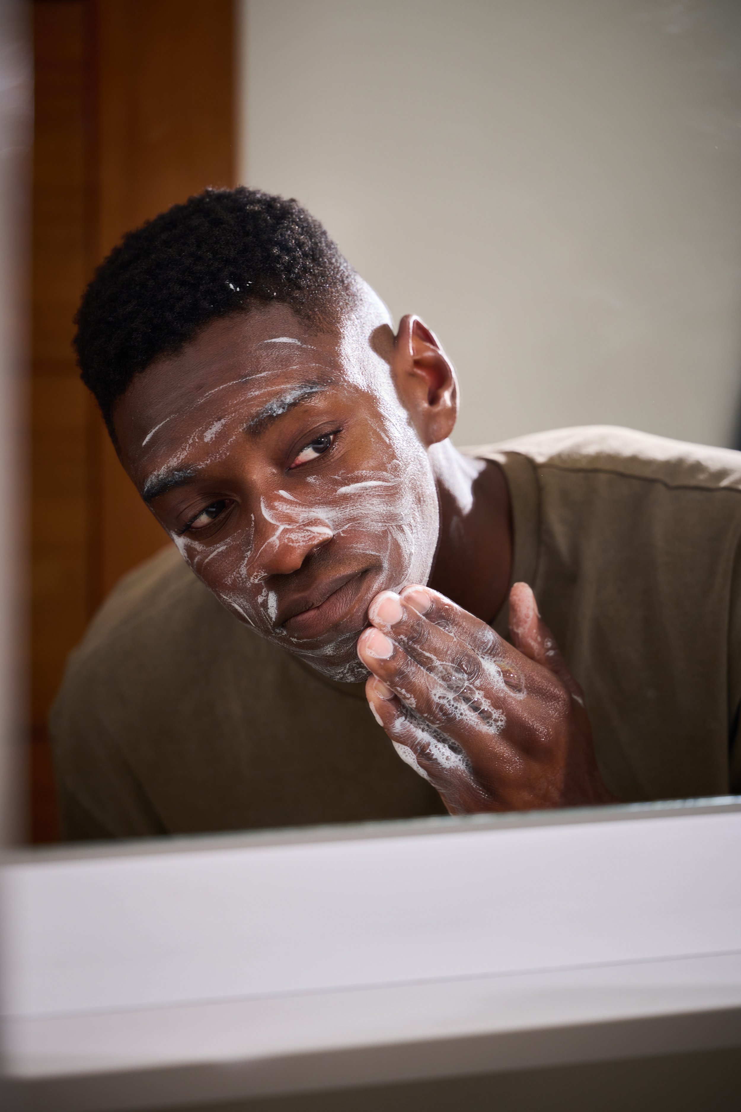 Man cleansing face in mirror during men's skincare routine tutorial shoot