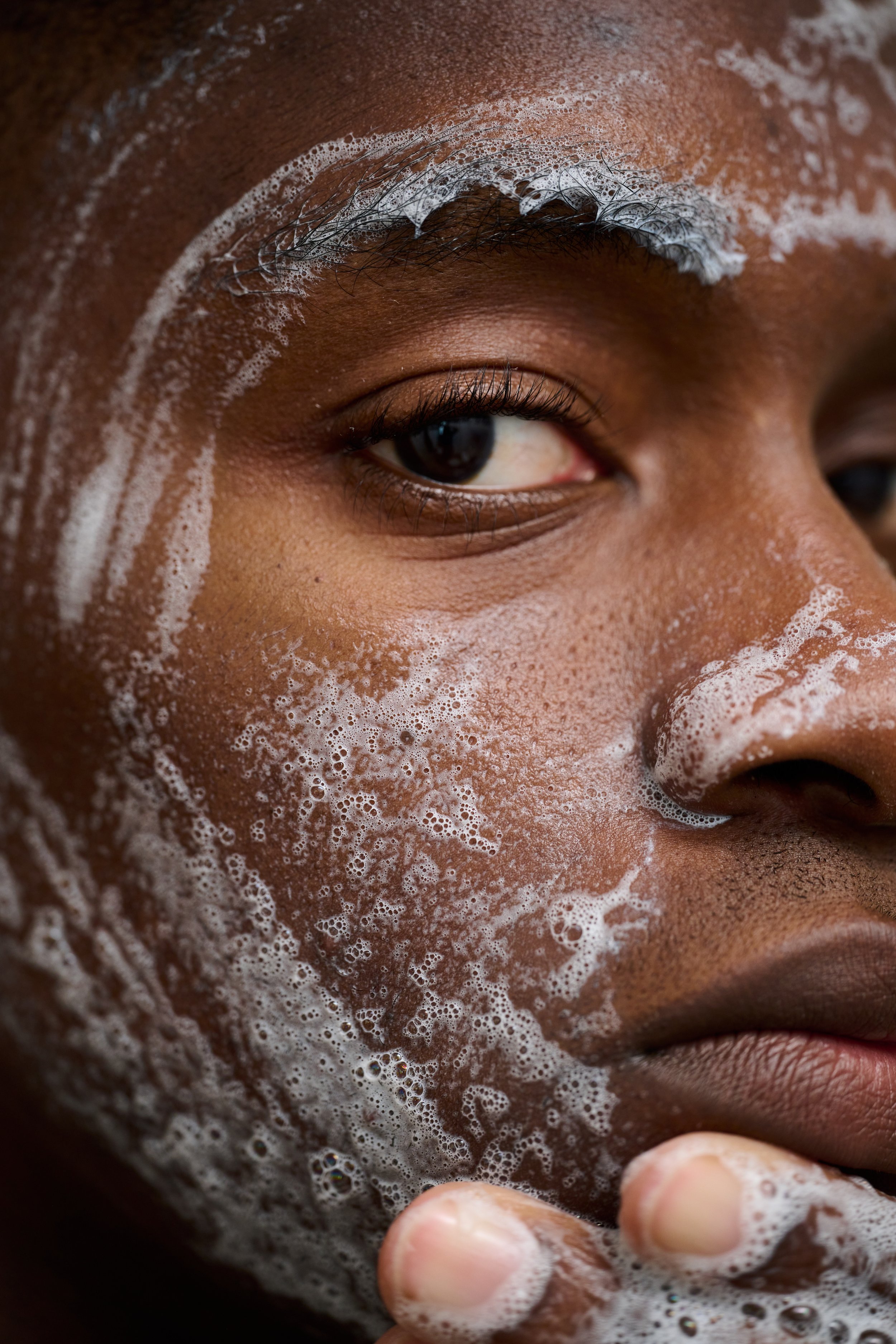 Close-up of Black man with cleanser on face looking into camera during men's skincare shoot