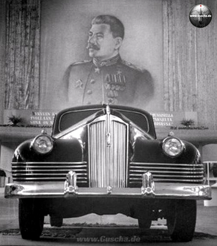 S/W-Bild eines ZIS-110 von vorne unten mit großem Stalinporträt im Hintergrund