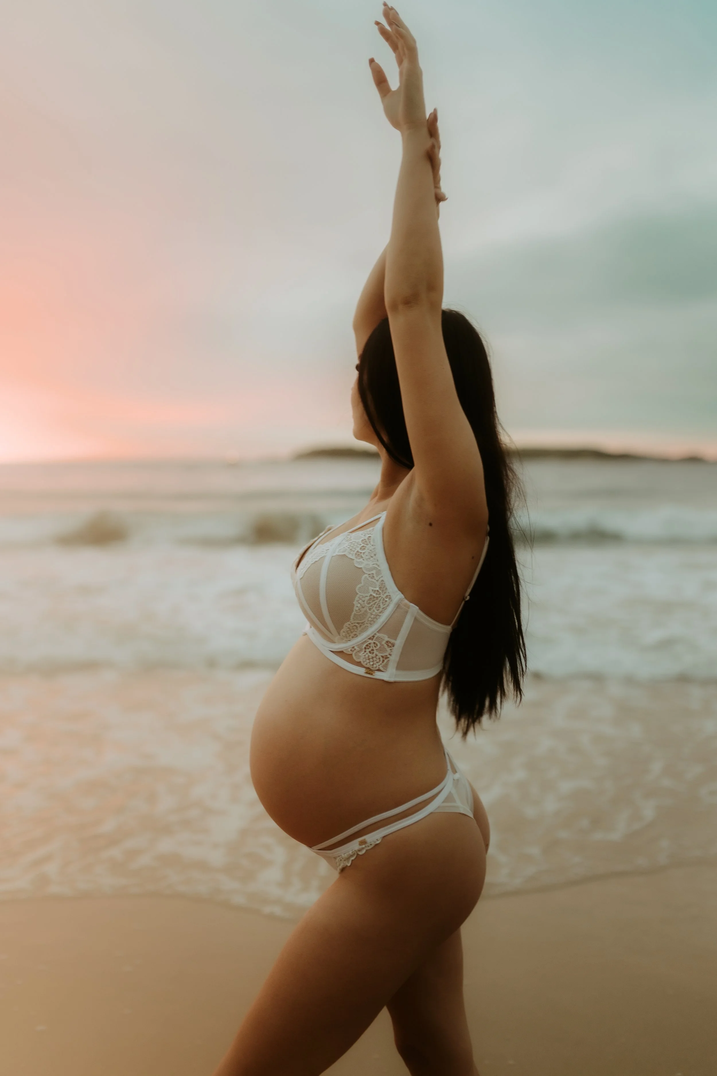 Pregnant woman in lingerie doing yoga on the beach at sunset.