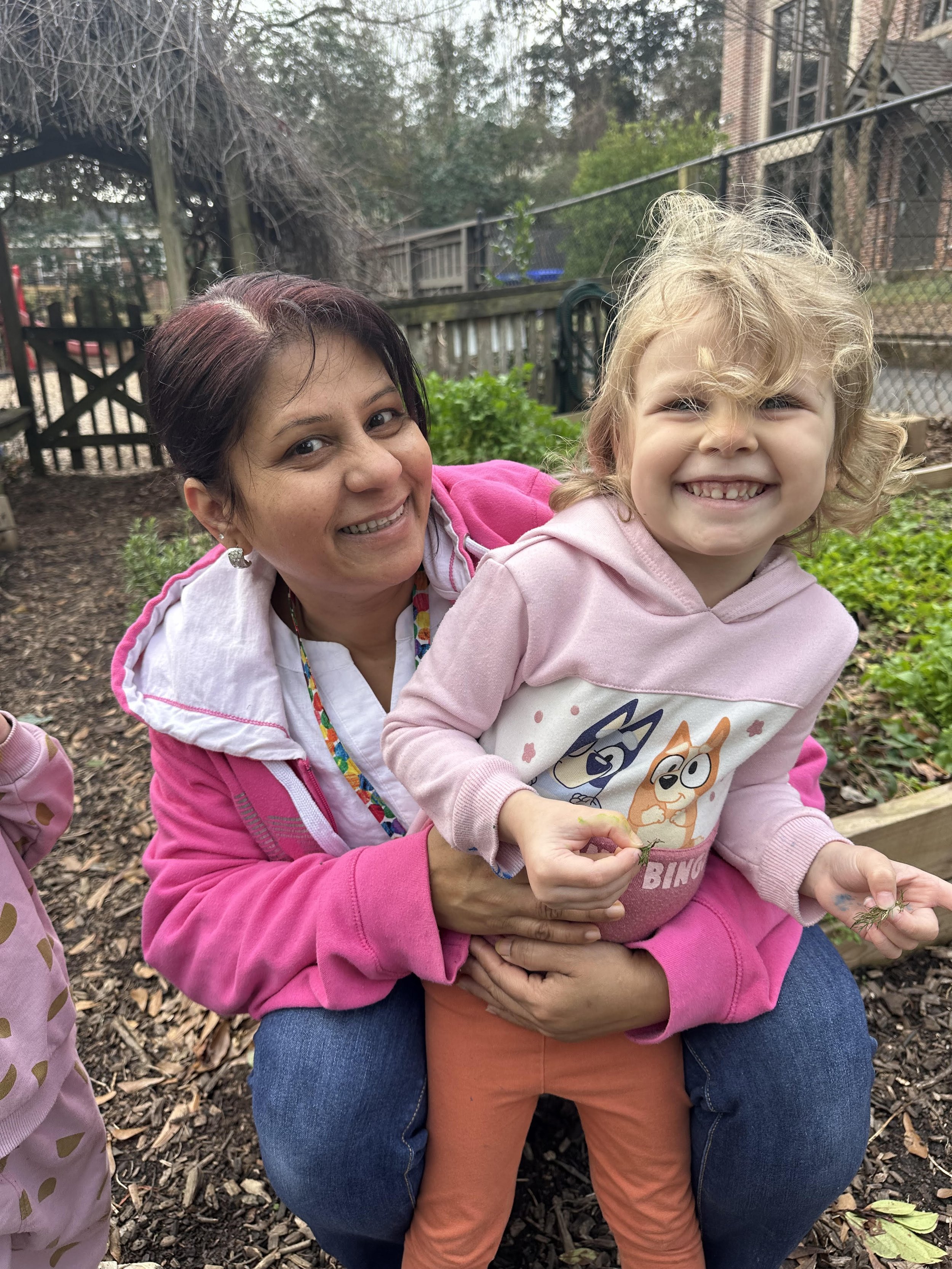 A teacher and student happily hug in the preschool garden