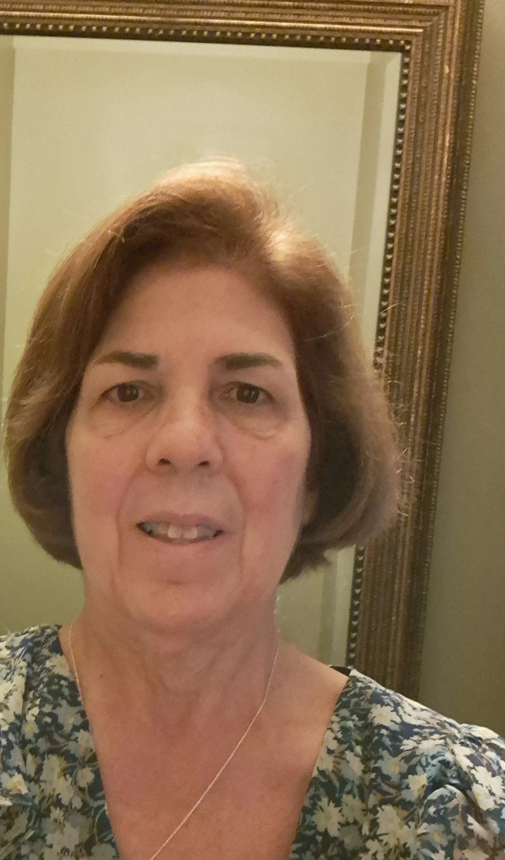 An older white woman with a light brown bob smiles in front of a green background