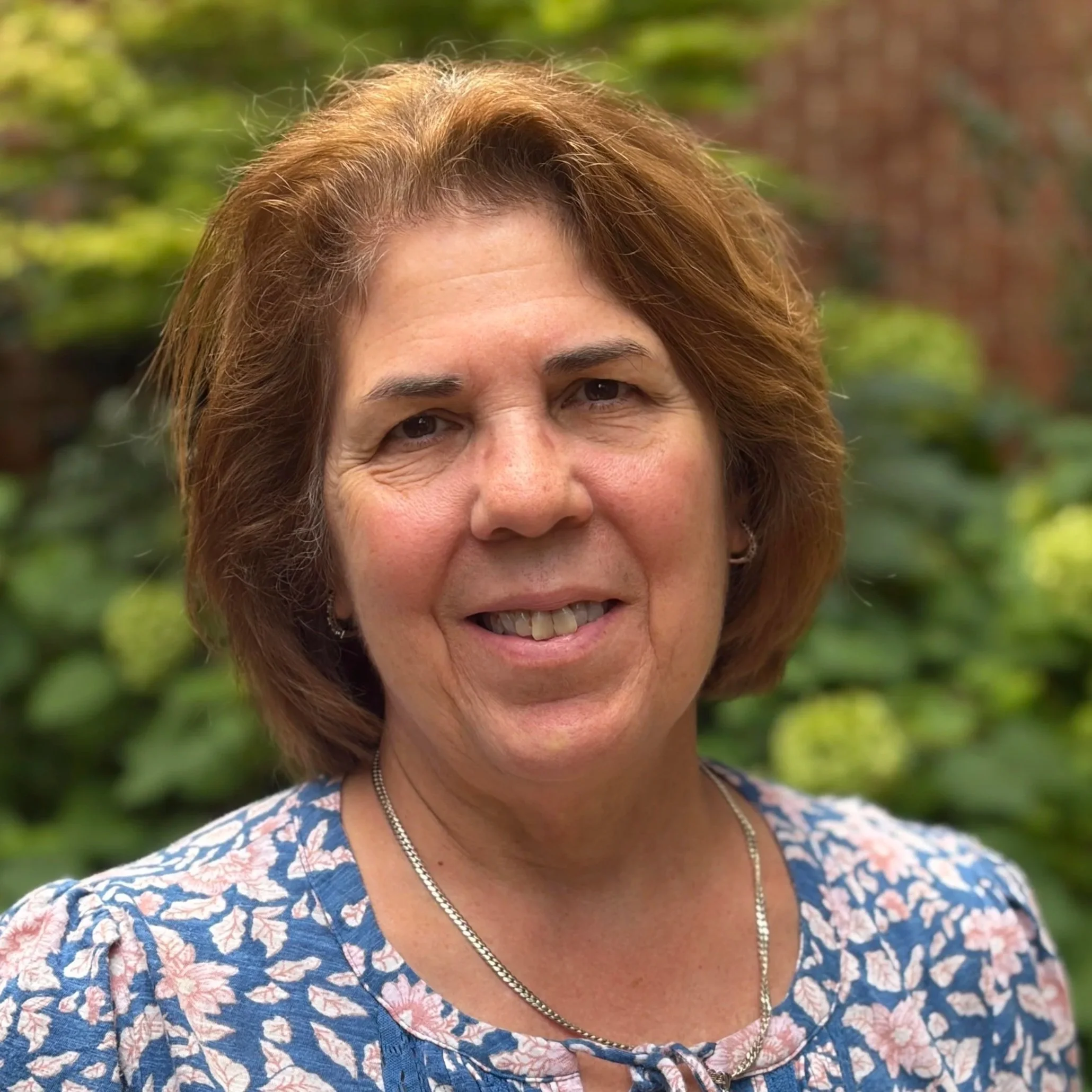 An older white woman with a light brown bob smiles  in front of a green background
