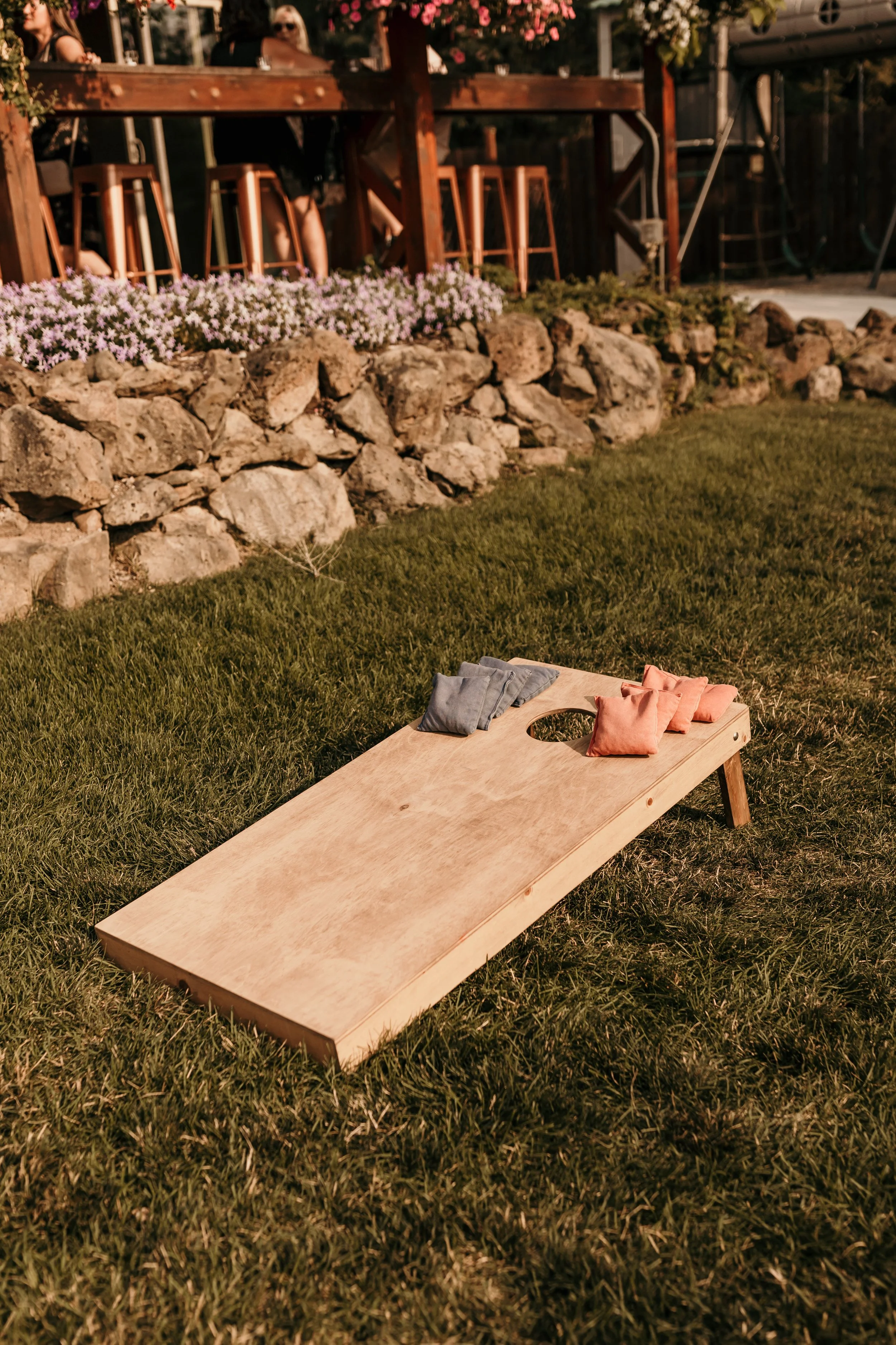 Wooden cornhole board with red and blue bean bags on a green lawn.