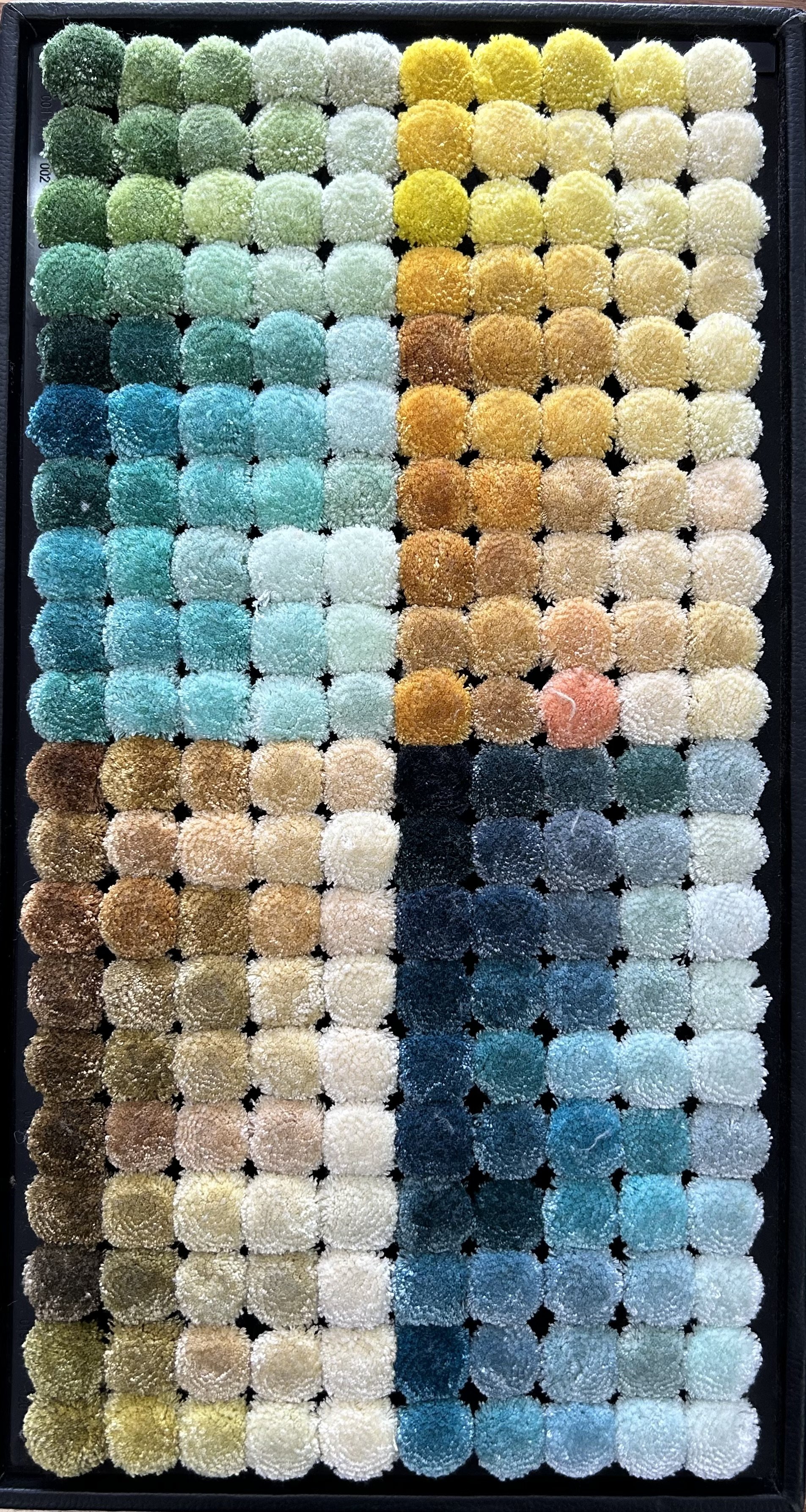 A grid of various colored yarn swatches, including shades of green, blue, yellow, brown, and beige, organized in a rectangular black frame.